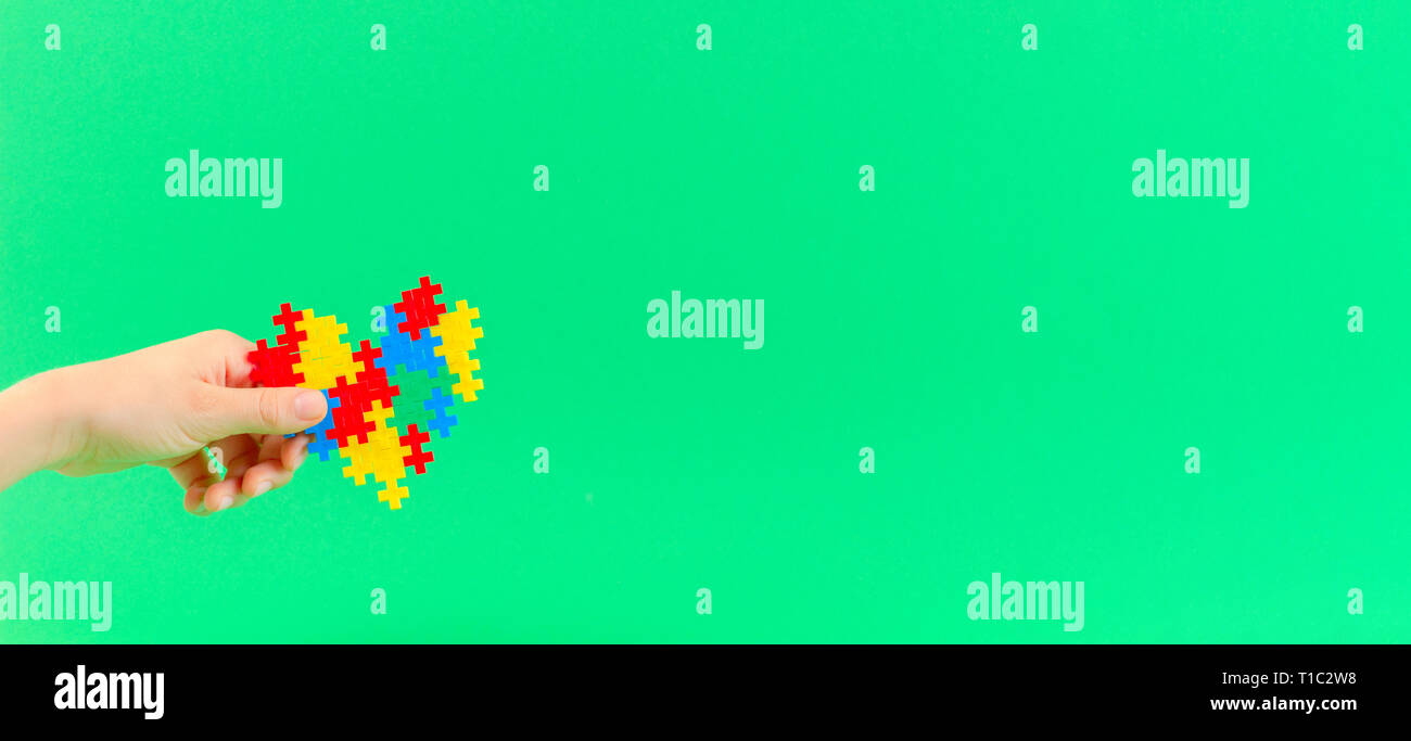 Bambino mano azienda cuore colorati su sfondo verde. Mondo autismo consapevolezza giorno di concetto Foto Stock