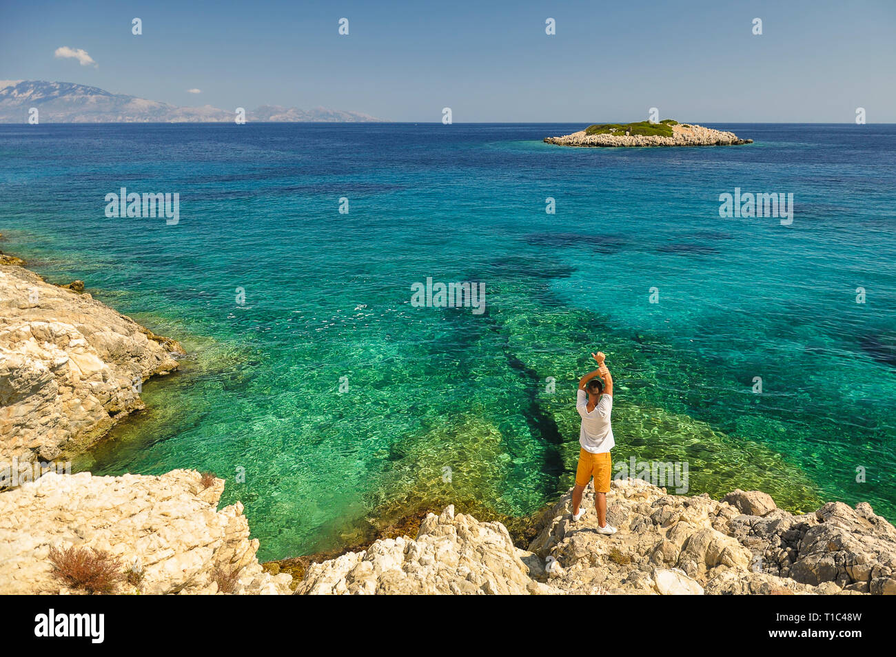 Paesaggio di vacanza dalla Grecia con vista sul blu di un mare Ionio con isola. Giovane maschio soggiorno turistico sulla costa mediterranea e mostrando il suo liberato Foto Stock