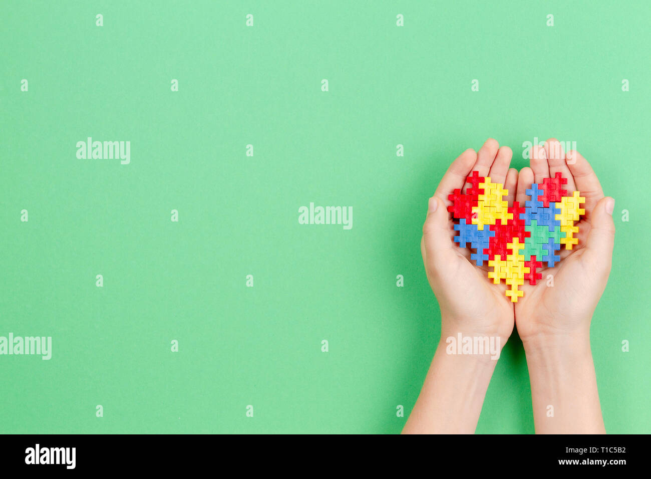 Bambino mano azienda cuore colorati su sfondo verde. Mondo autismo consapevolezza giorno di concetto Foto Stock