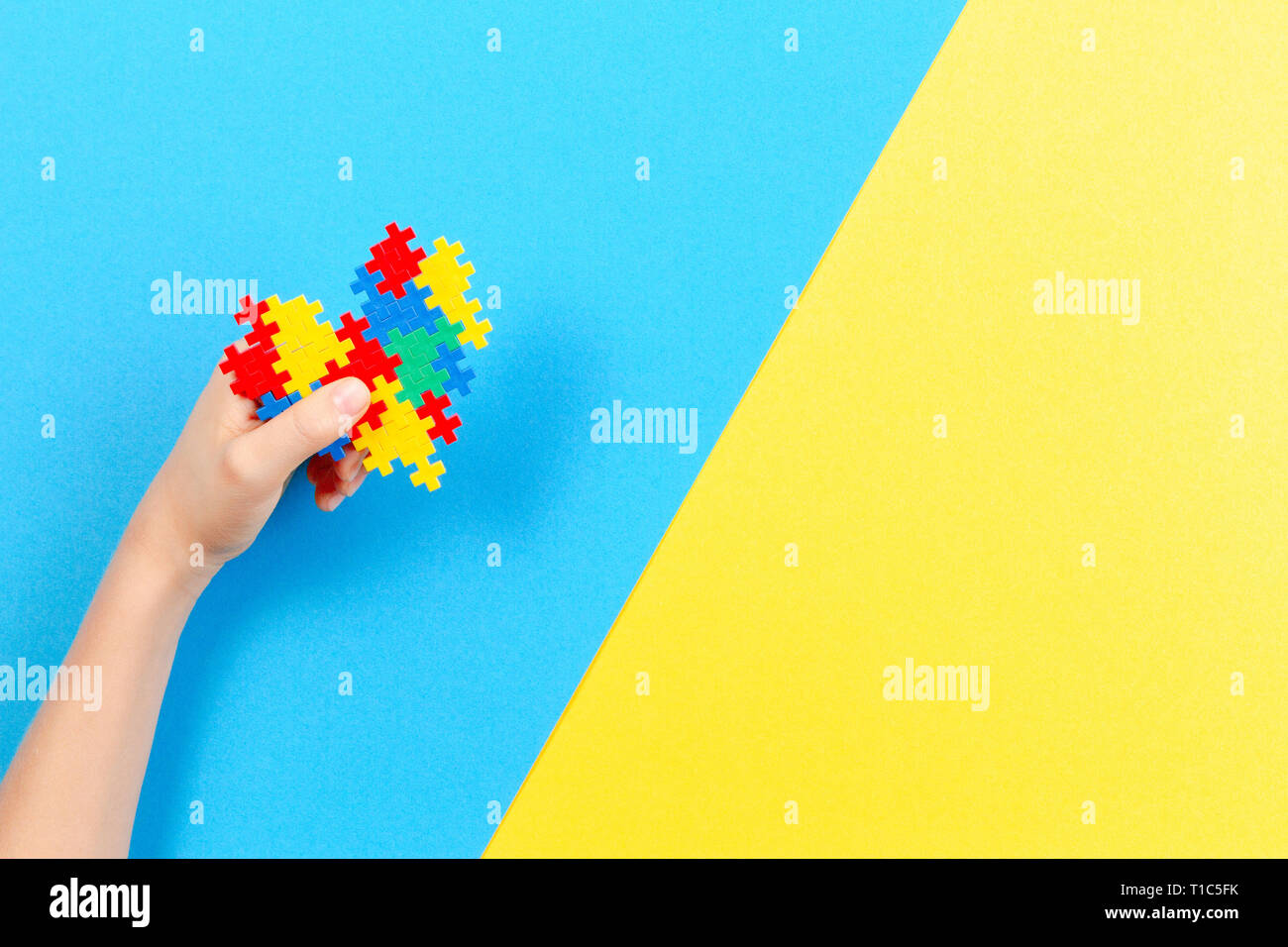 Bambino mano azienda cuore colorati in giallo e blu sullo sfondo. Mondo autismo consapevolezza giorno di concetto Foto Stock