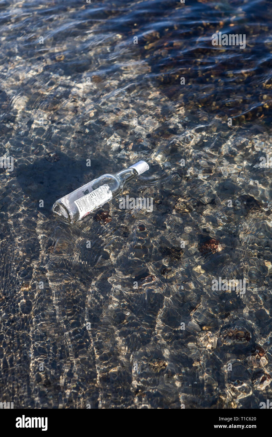 Alcol vuota bottiglia di vetro galleggiante in acqua di mare increspato Foto Stock