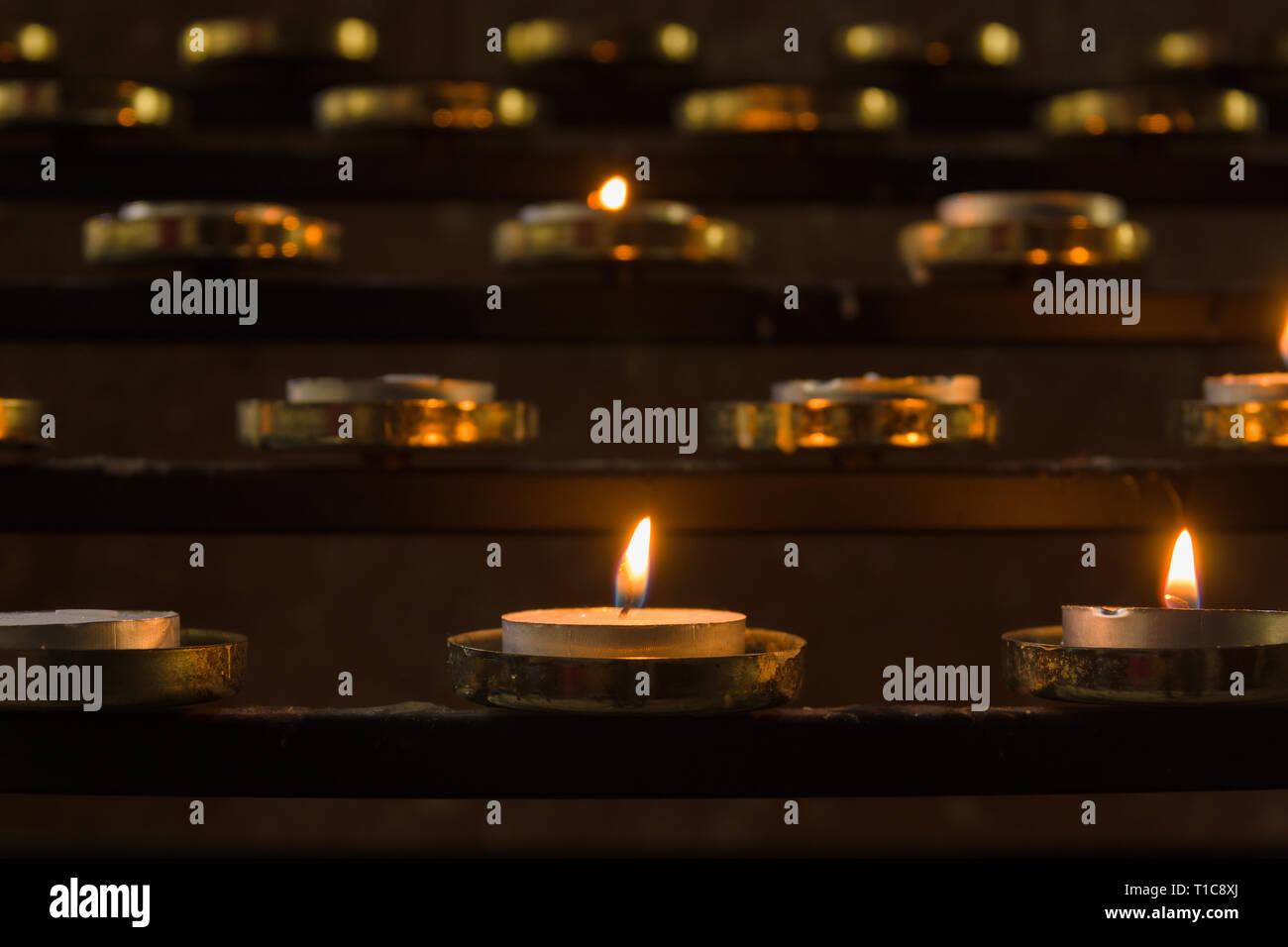 Candele votive illuminato come preghiere per i propri cari all'interno di una chiesa cristiana Foto Stock