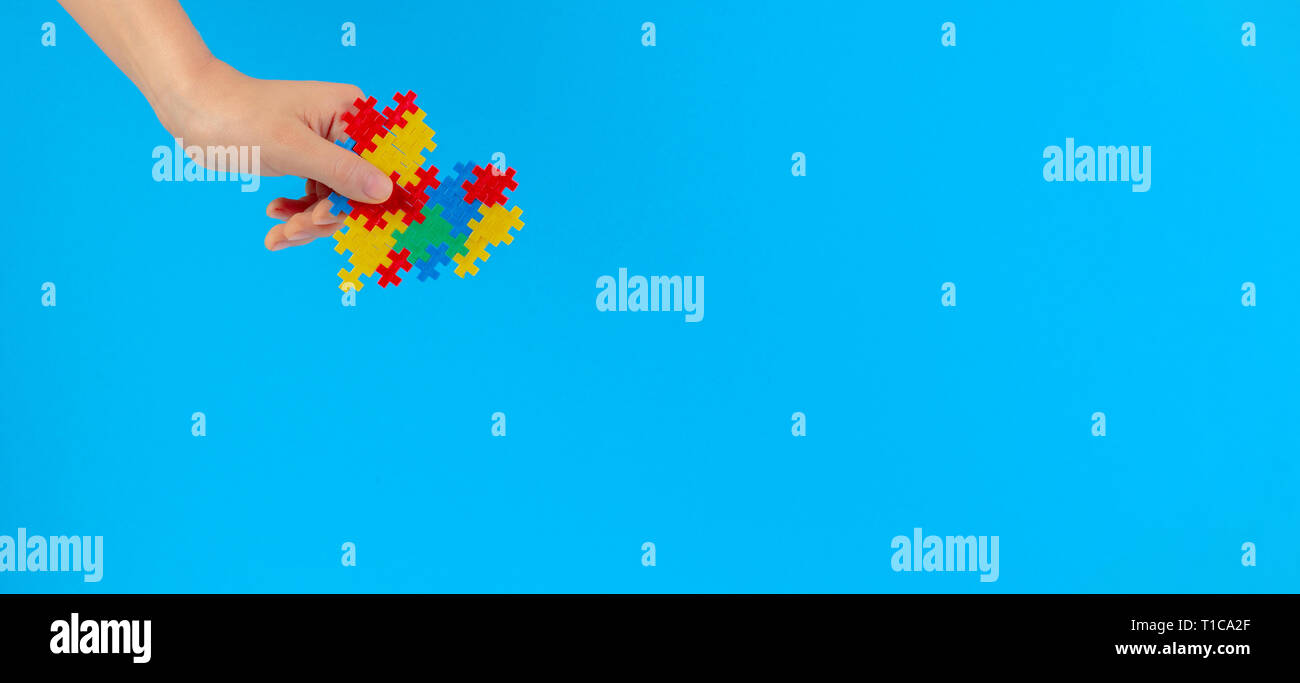Bambino mano azienda cuore colorati su sfondo blu. Mondo autismo consapevolezza giorno di concetto Foto Stock