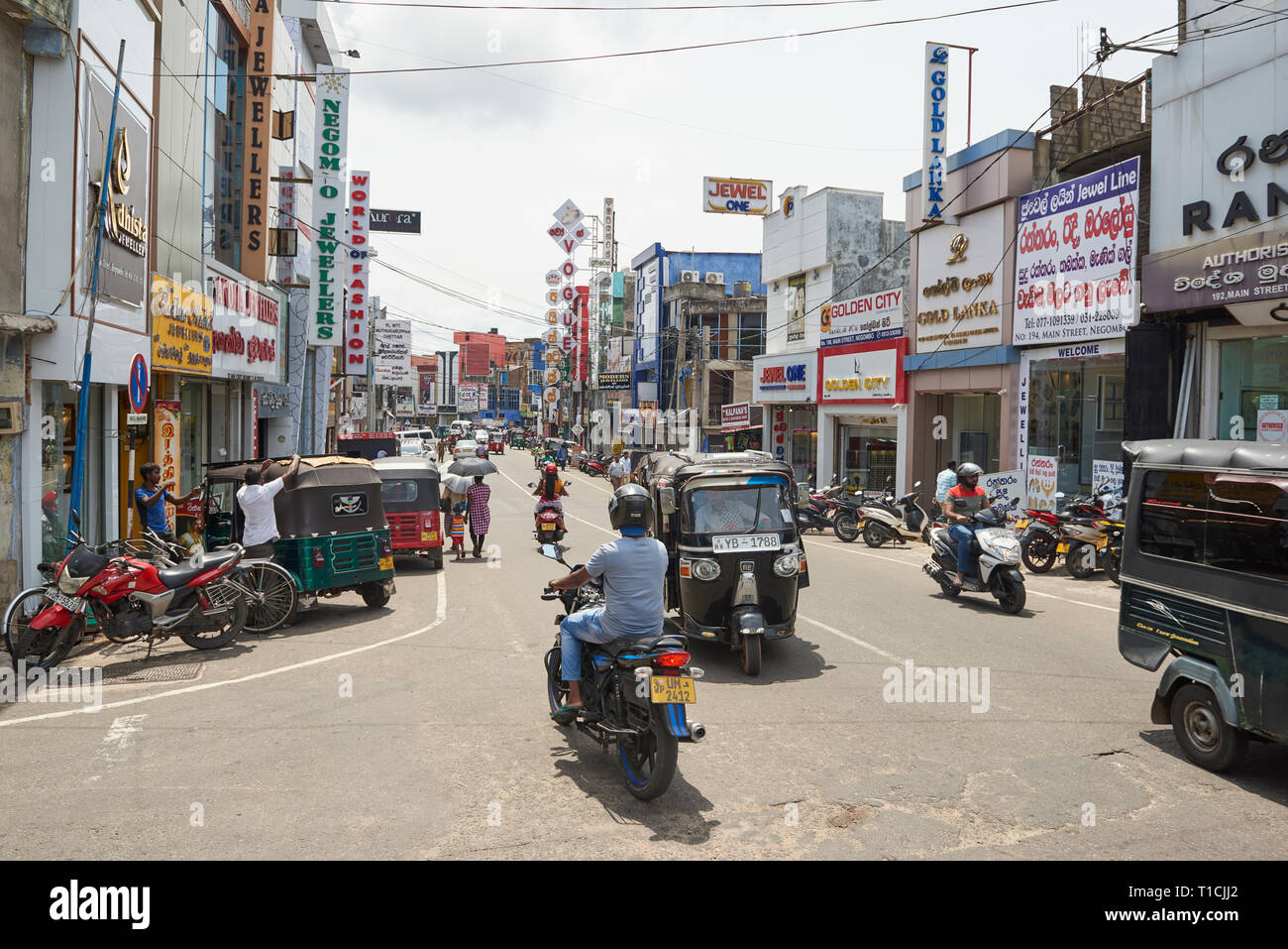 Occupato strada commerciale a Negombo, Sri Lanka, in una giornata di sole, con un traffico intenso di biciclette, auto, moto e tuk-tuks. Foto Stock