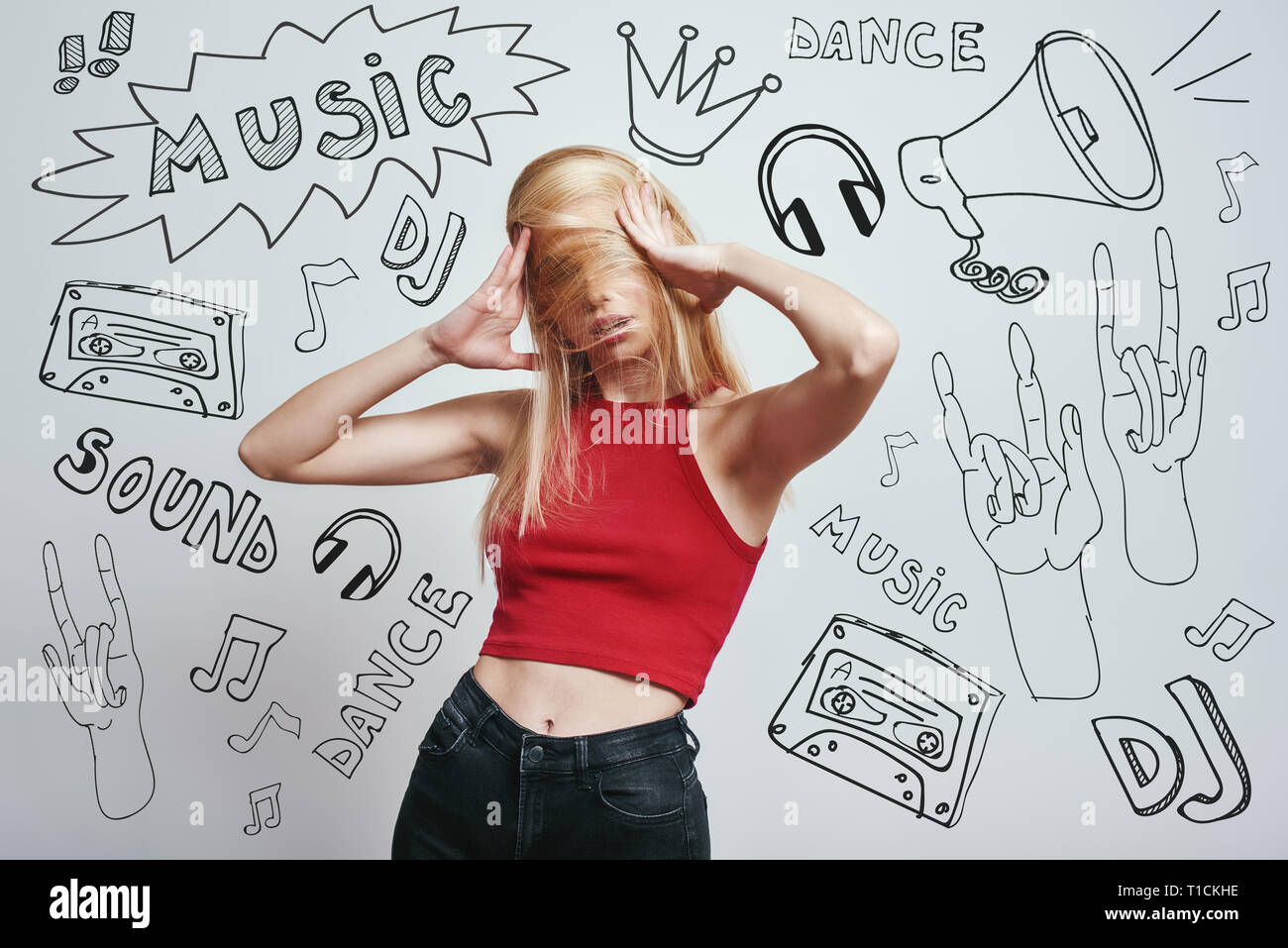 Funky umore. Close up ritratto giovane donna in rosso serbatoio superiore che ricopre la faccia con i suoi capelli mentre in piedi contro uno sfondo grigio con tema musicale scarabocchi. Foto Stock