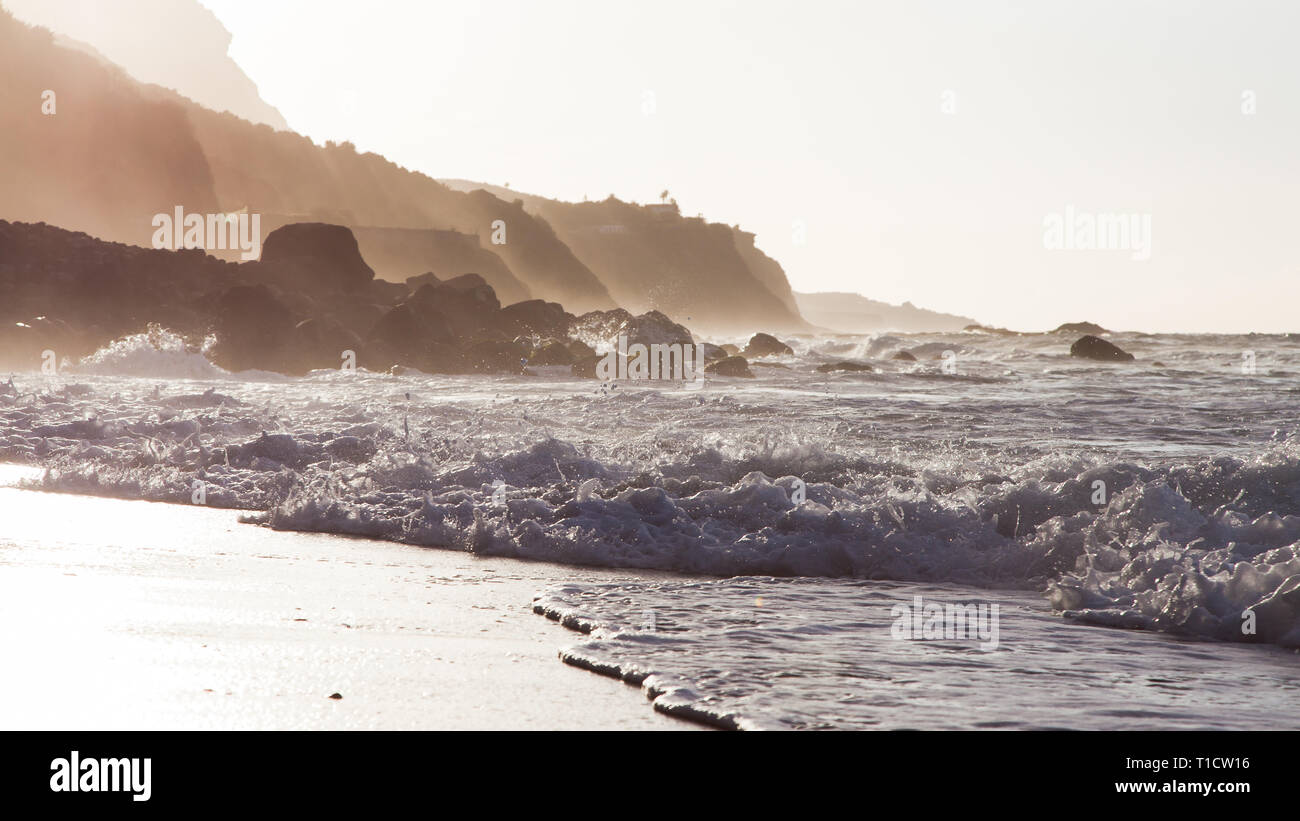 Onde che si infrangono e loro spray sulla riva di una spiaggia di Tenerife con indietro luce del tramonto che sopraggiungono in primavera . Foto Stock