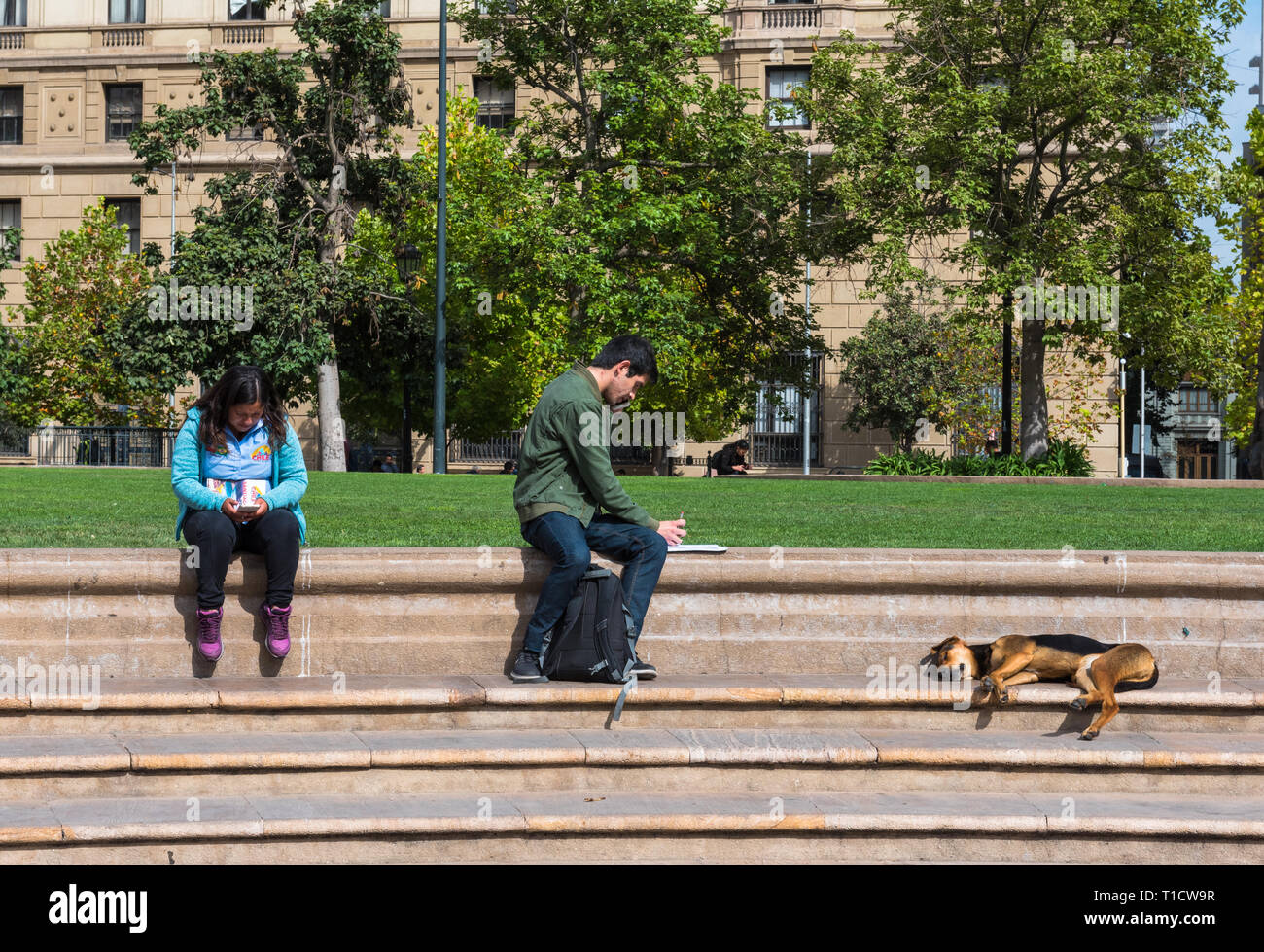 Santiago del Cile--Aprile 6, 2018. Due persone sono seduti sui passi da un parco mentre un cane dorme nelle vicinanze. Foto Stock