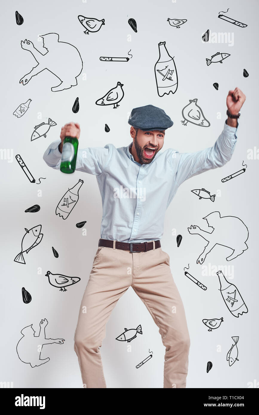 Parte! Ubriaco uomo brutale in hat tenendo una birra e urlando mentre in piedi contro uno sfondo grigio con disegnati a mano scarabocchi su di esso. Concetto di mafia Foto Stock