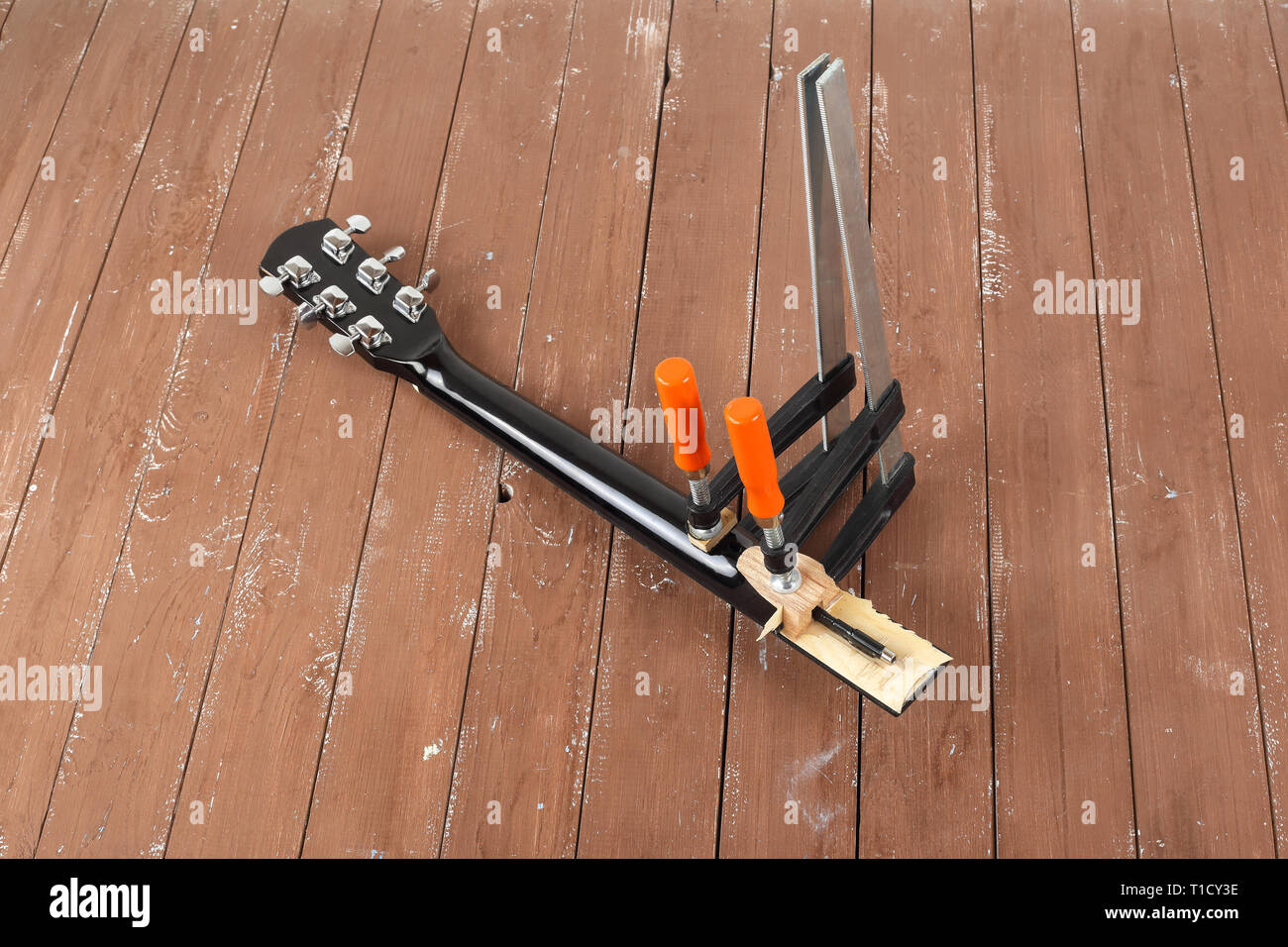 La riparazione di una chitarra e il servizio di assistenza - il serraggio di una chitarra collo sfondo di legno Foto Stock