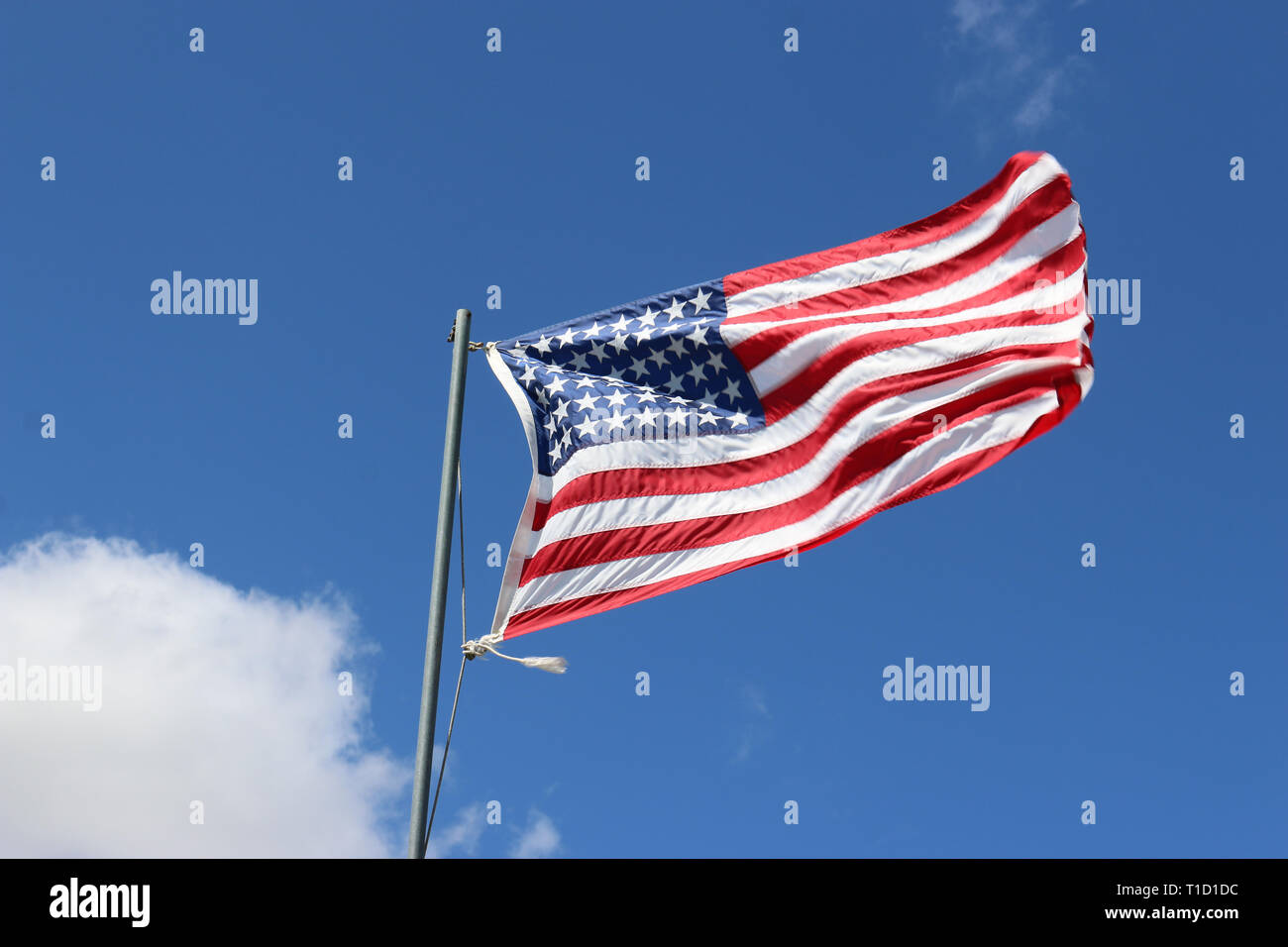 Stelle e strisce della bandiera nazionale degli Stati Uniti d'America battenti e svolazzanti su un polo grigia con cielo blu e nuvole bianche in background. Foto Stock