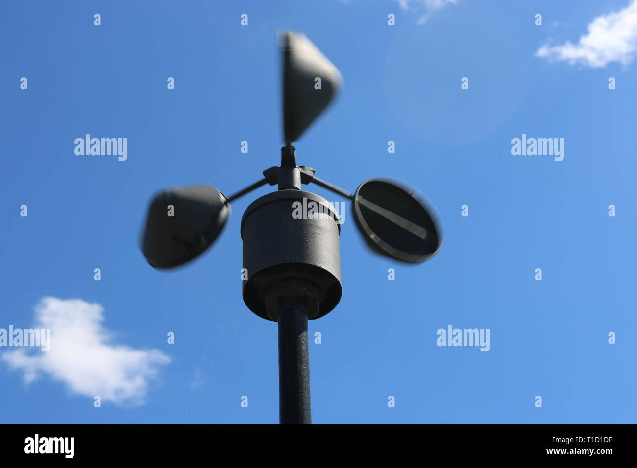 Spostando la velocità del vento indicatore, anemometro, sulla sommità di un palo e sfocate con movimento con cielo blu e nuvole bianche in background. Foto Stock