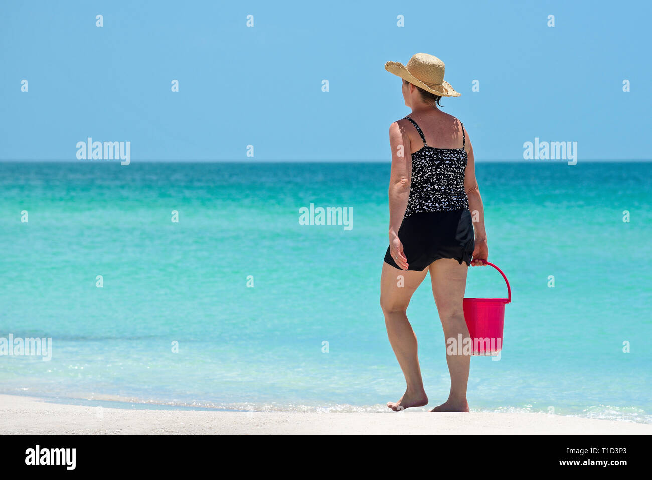 Donna che cammina sulla Gulf Coast Beach in Florida che porta una spiaggia rossa la benna Foto Stock