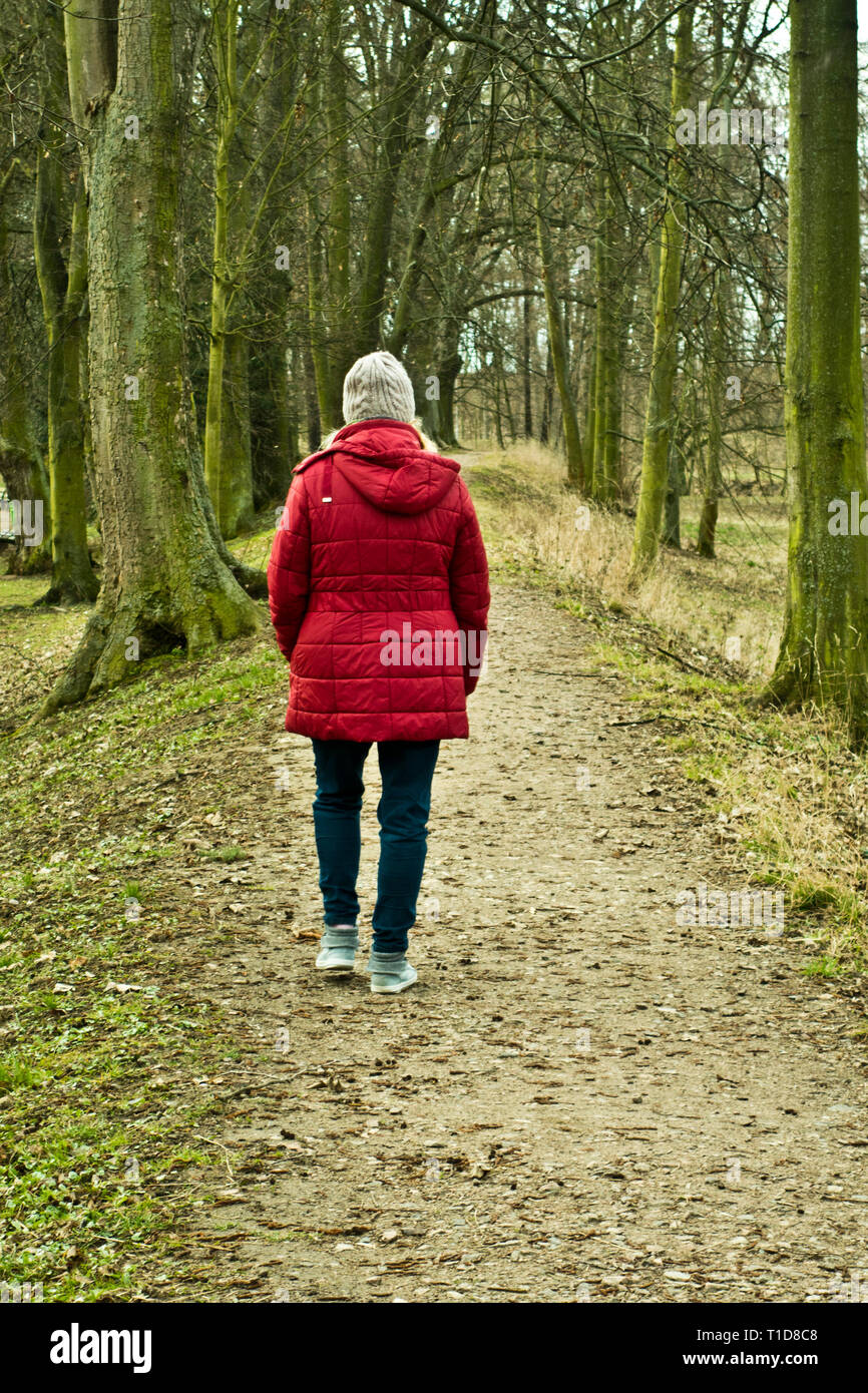 Woman in Red coat camminare da solo lungo un percorso nella natura Foto Stock