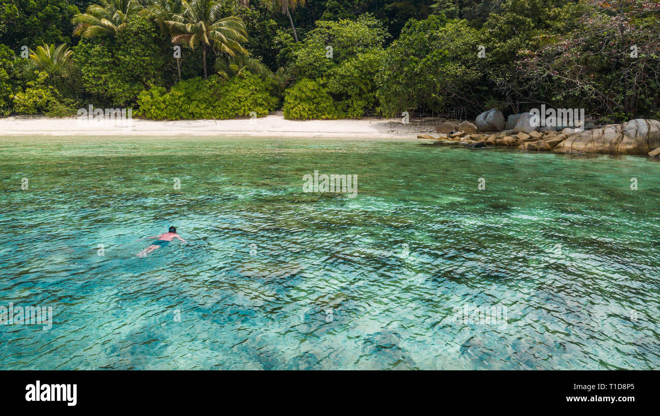 L uomo lo snorkeling in un mare tropicale vicino alla spiaggia sabbiosa e la giungla in Perhentian Island. Vacanze a destinazione di viaggio in Asia. Foto Stock
