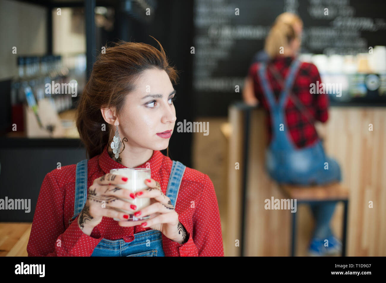 Ragazza giovane e carina nel quartiere alla moda di costume di denim con bicchiere di caffè bianco in seduta coffeehouse Foto Stock