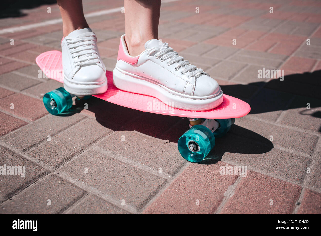 Close up girl per le gambe e piedi indossa sneakers bianco. Ragazza è standin sul pattino rosa con entrambi i piedi. Vi è una giornata di sole al di fuori. Foto Stock