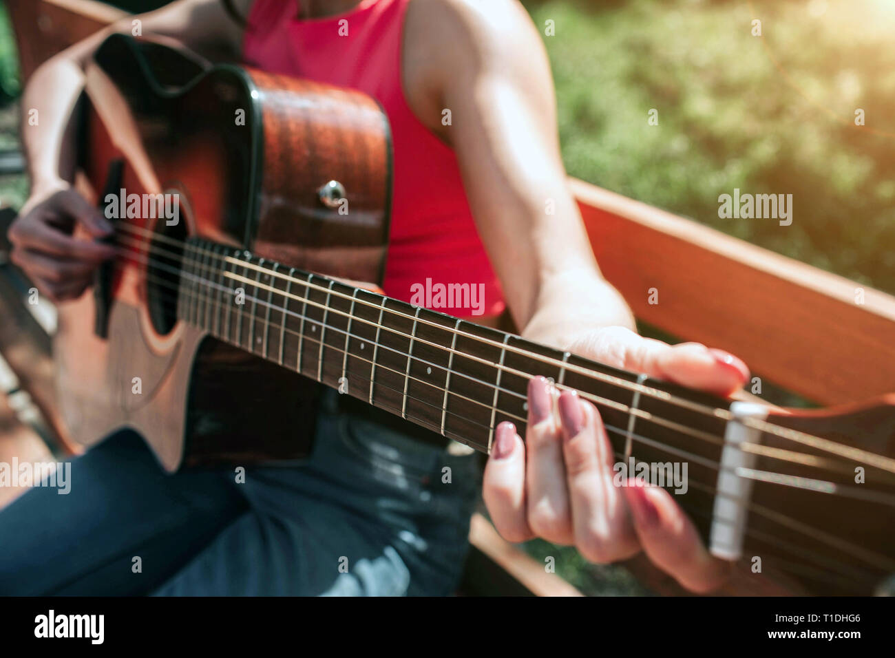 Close up di musicista con le mani in mano a suonare la chitarra. Ragazza sta tenendo le sue dita sulla chitarra di stringhe. La ragazza è seduta sul banco di lavoro al di fuori di questa bella Foto Stock