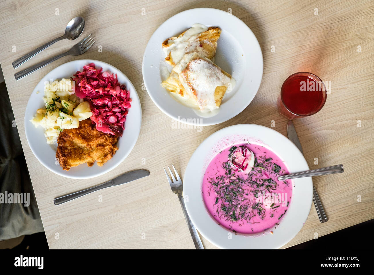 Il pranzo presso il Bar Bambino, Varsavia, Polonia - chlodnik, un bicchiere di kompot, maiale fritto chop con cavolo e patate imburrato e mirtillo frittelle. Foto Stock