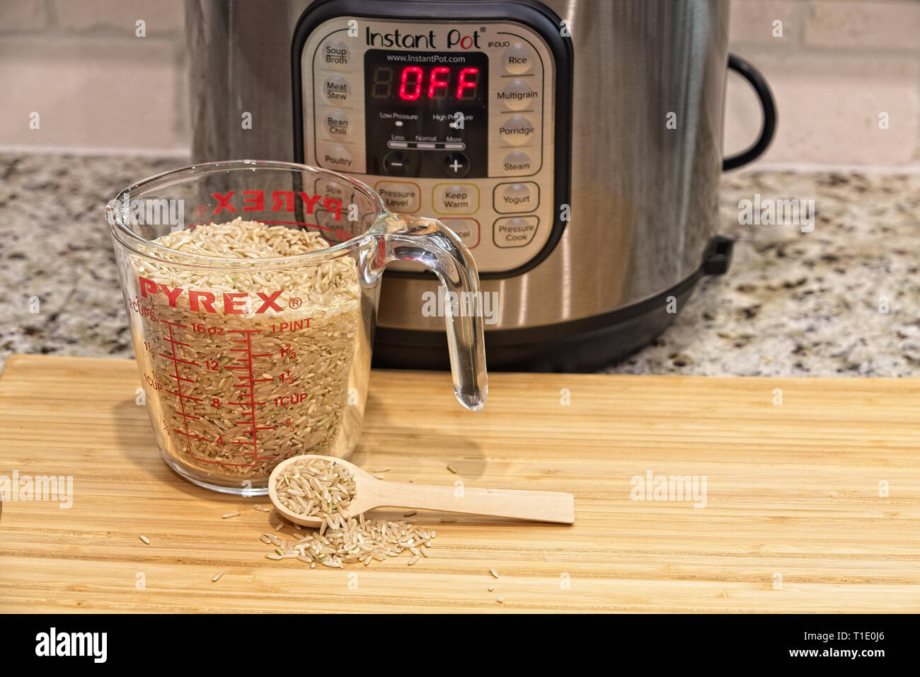 Un cucchiaio e una tazza di riso marrone su un legno tagliere e un istante Pot in background Foto Stock