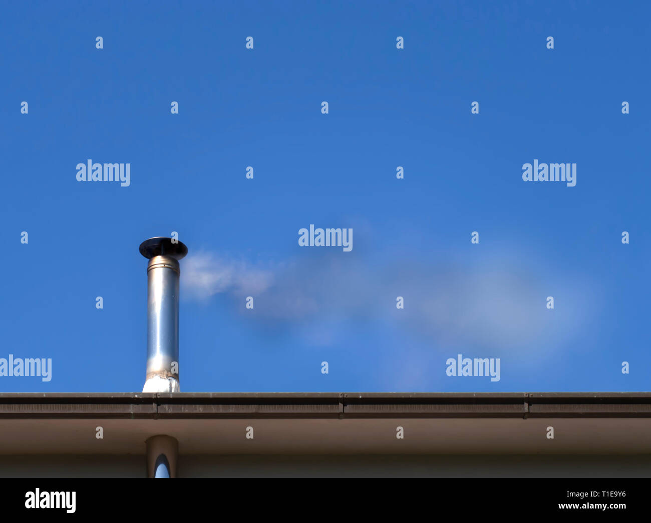 Il fumo e il problema dell'inquinamento da una stufa a legna camino, in blu luminoso cielo estivo. Foto Stock