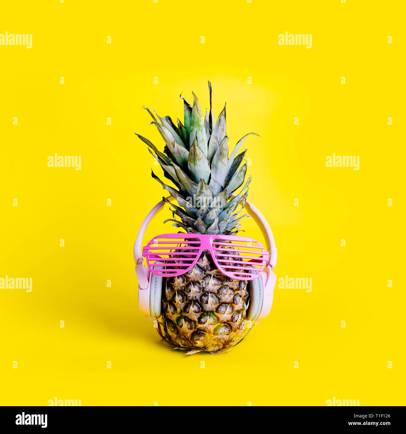 Moda alla moda di ananas frutta con cuffie e occhiali da sole per ascoltare la musica su pastello luminoso sfondo giallo. Cool Parigamba con ananas Foto Stock