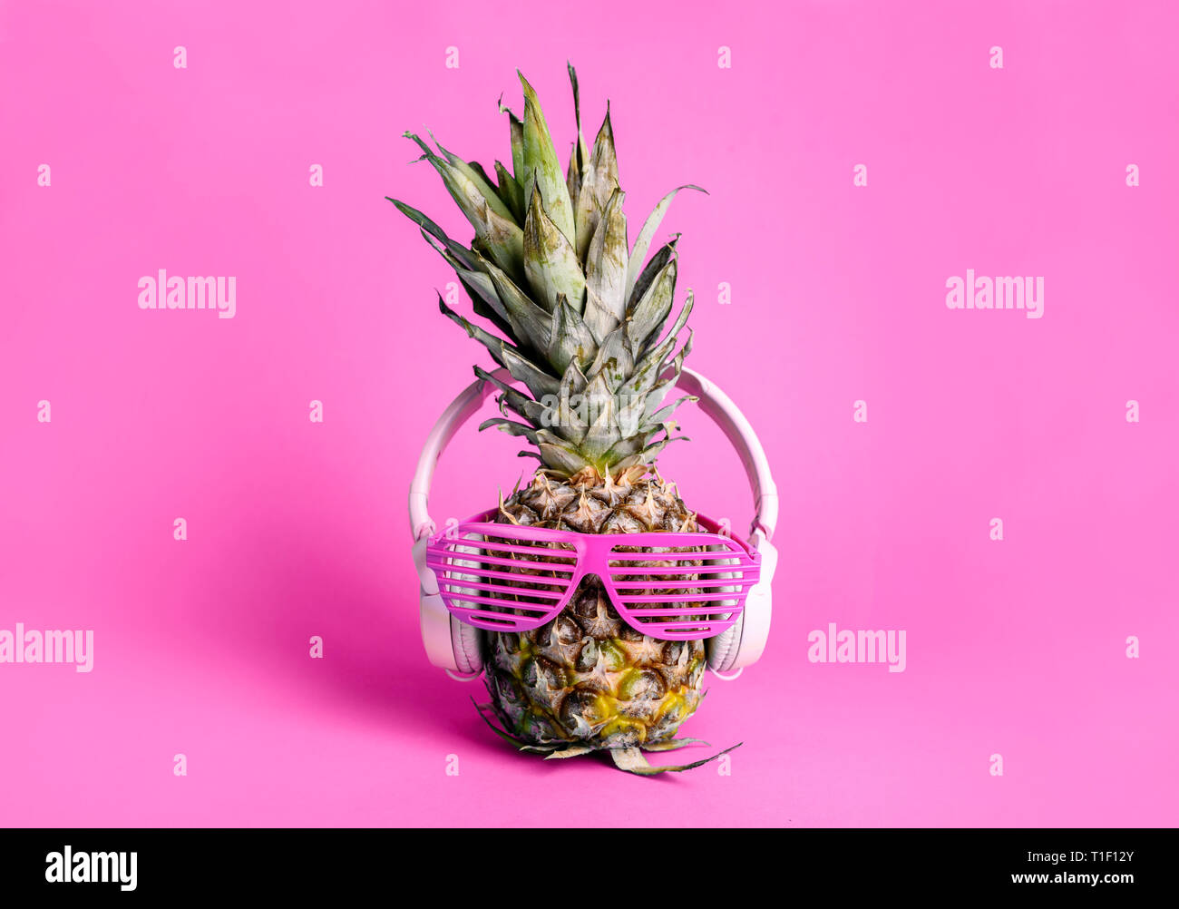 Moda alla moda di ananas frutta con cuffie e occhiali da sole per ascoltare la musica su pastello luminoso sfondo rosa. Cool Parigamba ananas con f Foto Stock