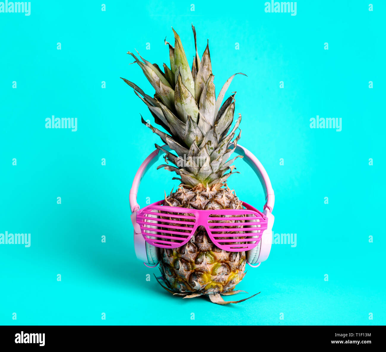 Moda alla moda di ananas frutta con cuffie e occhiali da sole per ascoltare la musica su pastello luminoso sfondo ciano. Cool Parigamba ananas con f Foto Stock