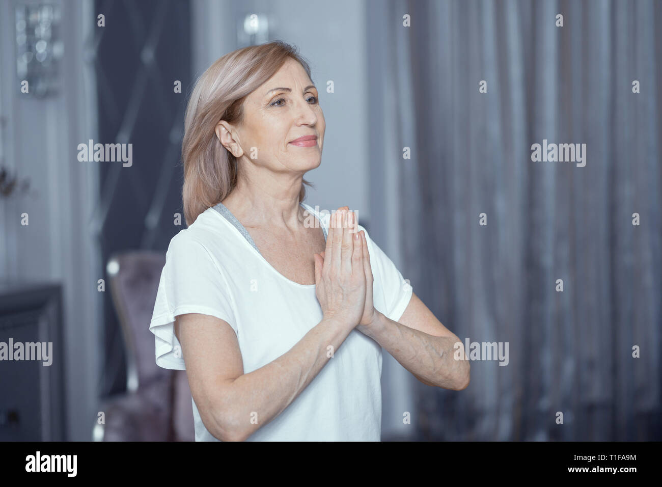 Donna 50 o 60 anni facendo Yoga Folding le mani davanti a lui. Foto Stock
