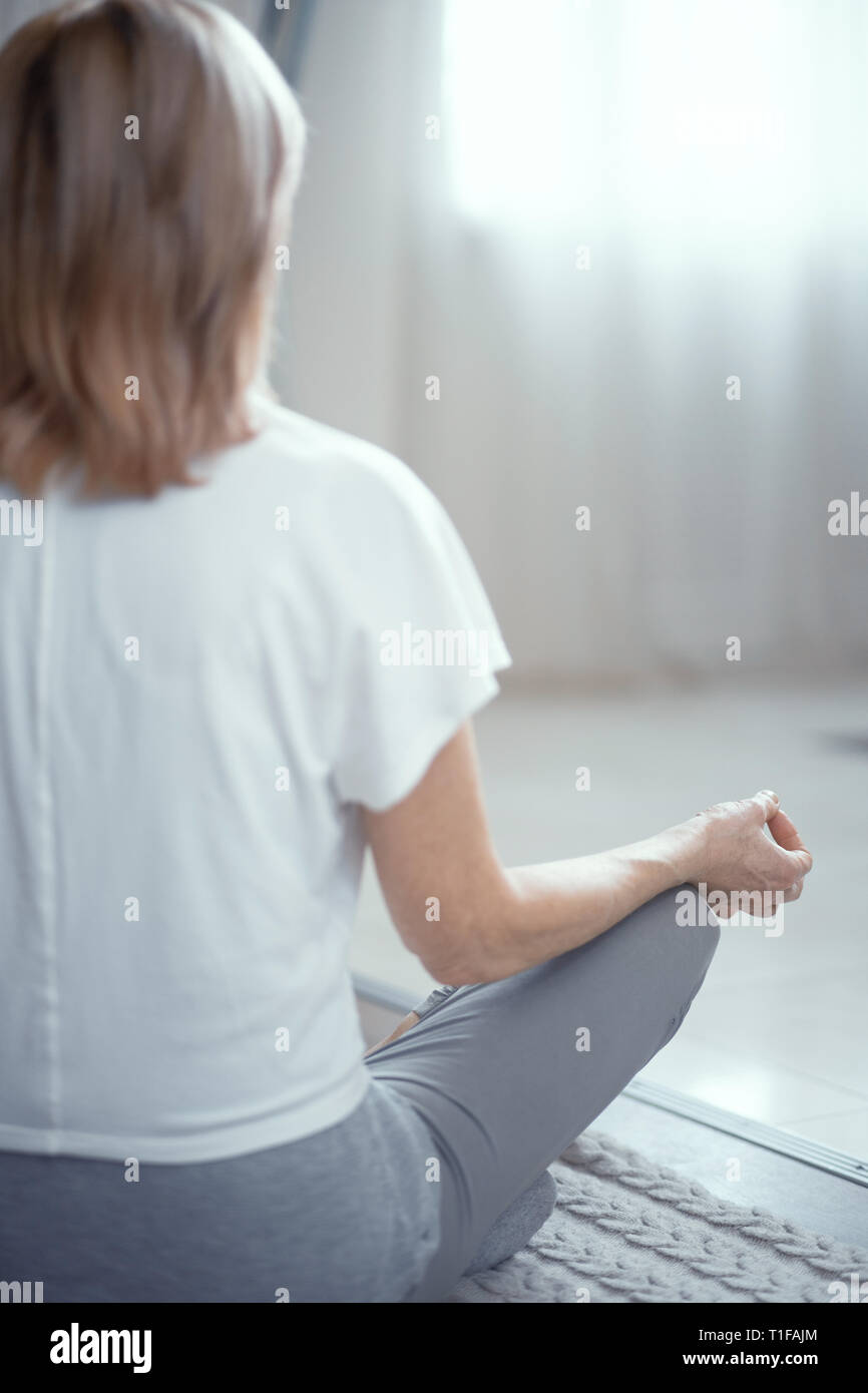 Donna matura seduta sul pavimento nella posizione del loto Foto Stock