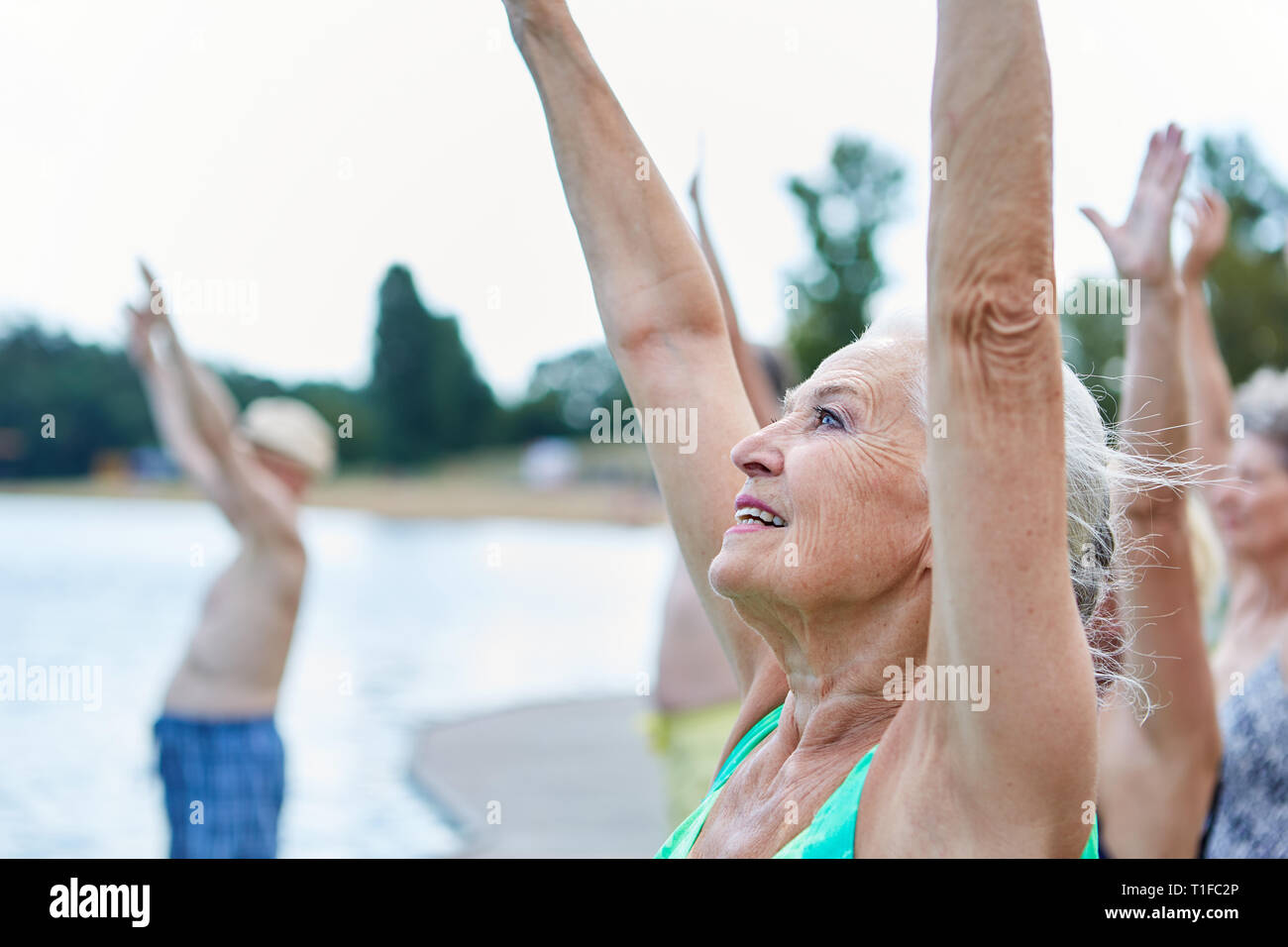 Senior donna stretching con il suo retro gruppo di addestramento in riabilitazione al lago Foto Stock