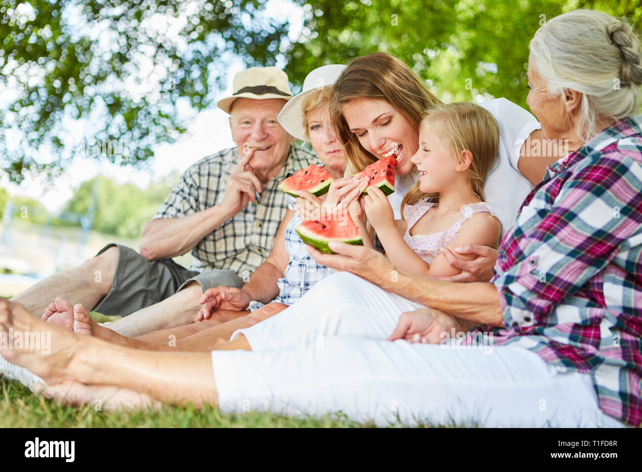 Famiglia estesa con i nonni e la figlia di mangiare il melone rilassante nel parco Foto Stock