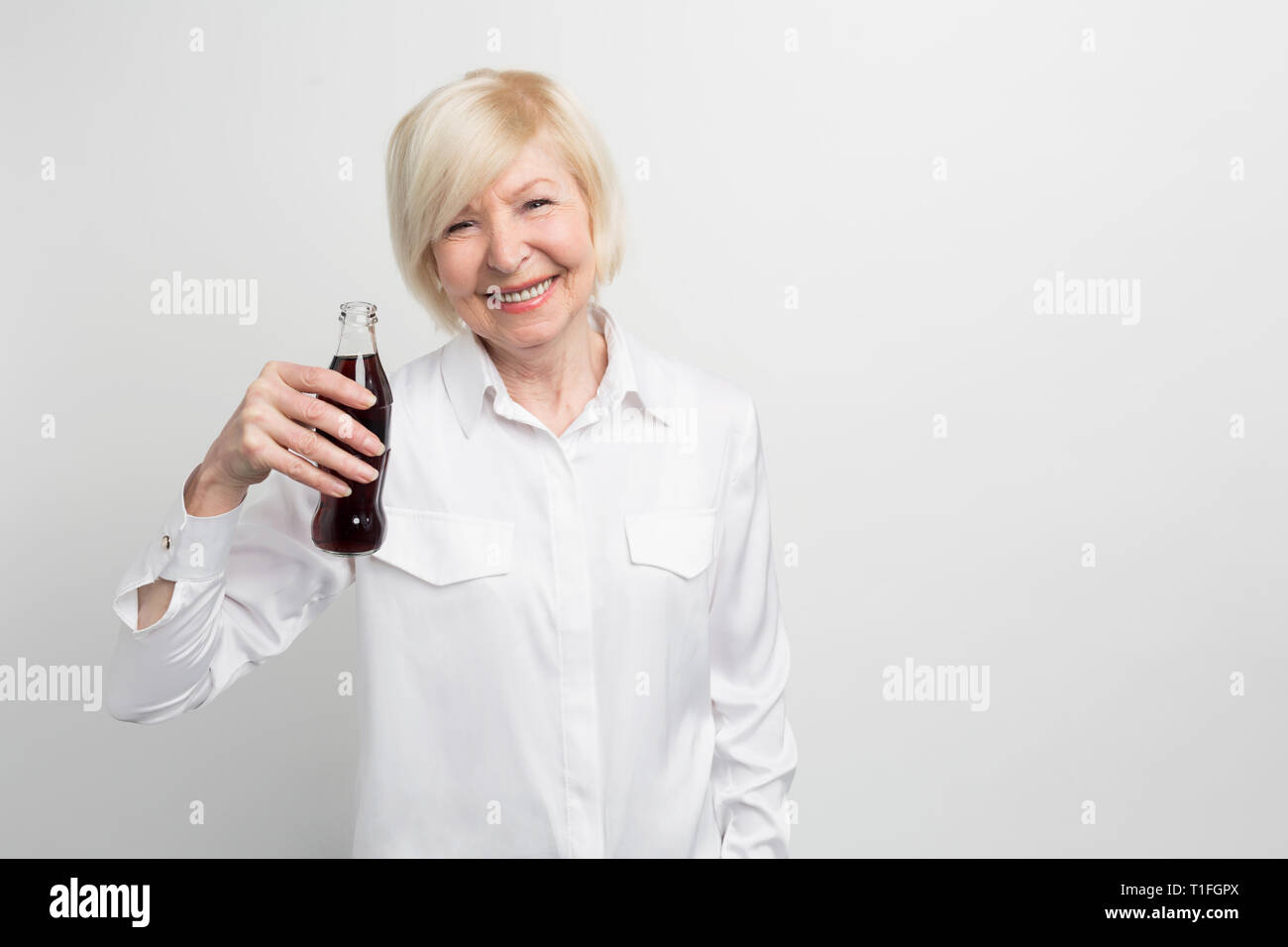 Una foto della vecchia donna degustazione coca cola. Lei come questa bevanda in quanto l'infanzia. Non è sano bere ma ama. Isolato su bianco Foto Stock