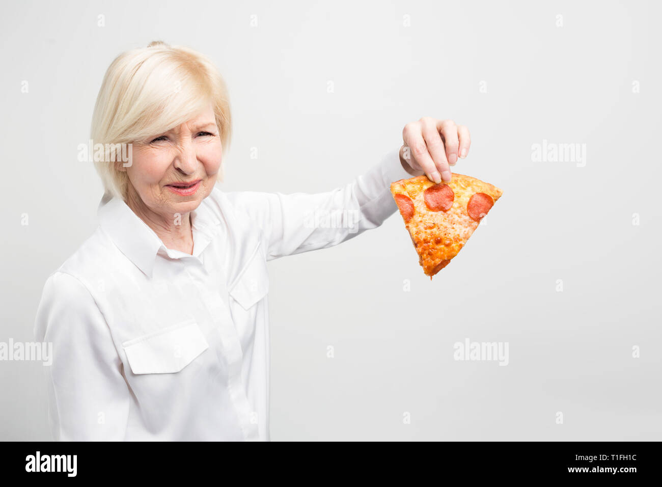 La nonna non piace l'idea di mangiare questo pezzo di pizza perché non è buona e helthy per gli esseri umani. Isolato su sfondo bianco. Foto Stock