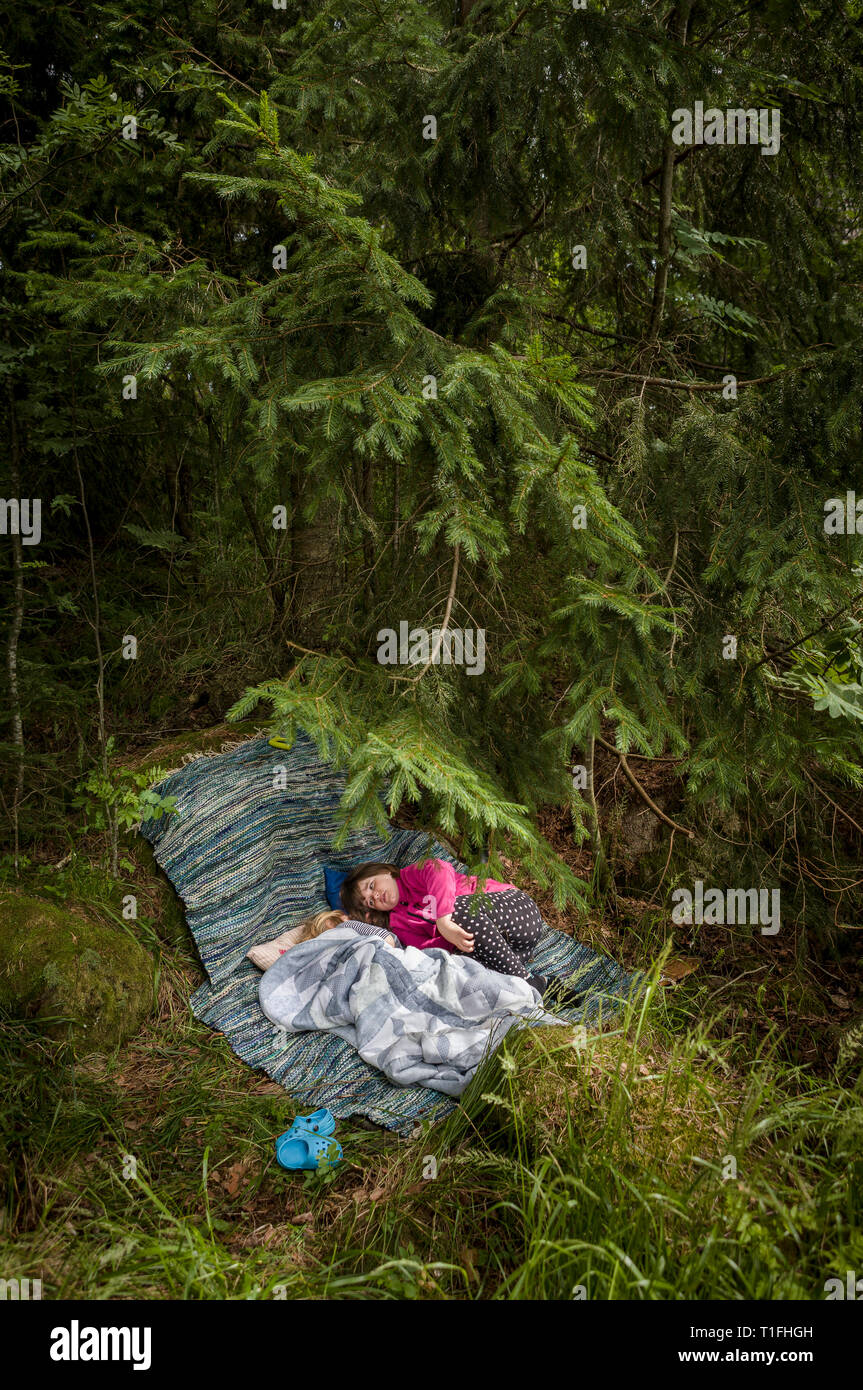 Tho ragazze in appoggio in corrispondenza di un accampamento sotto un pino nella foresta. Foto Stock