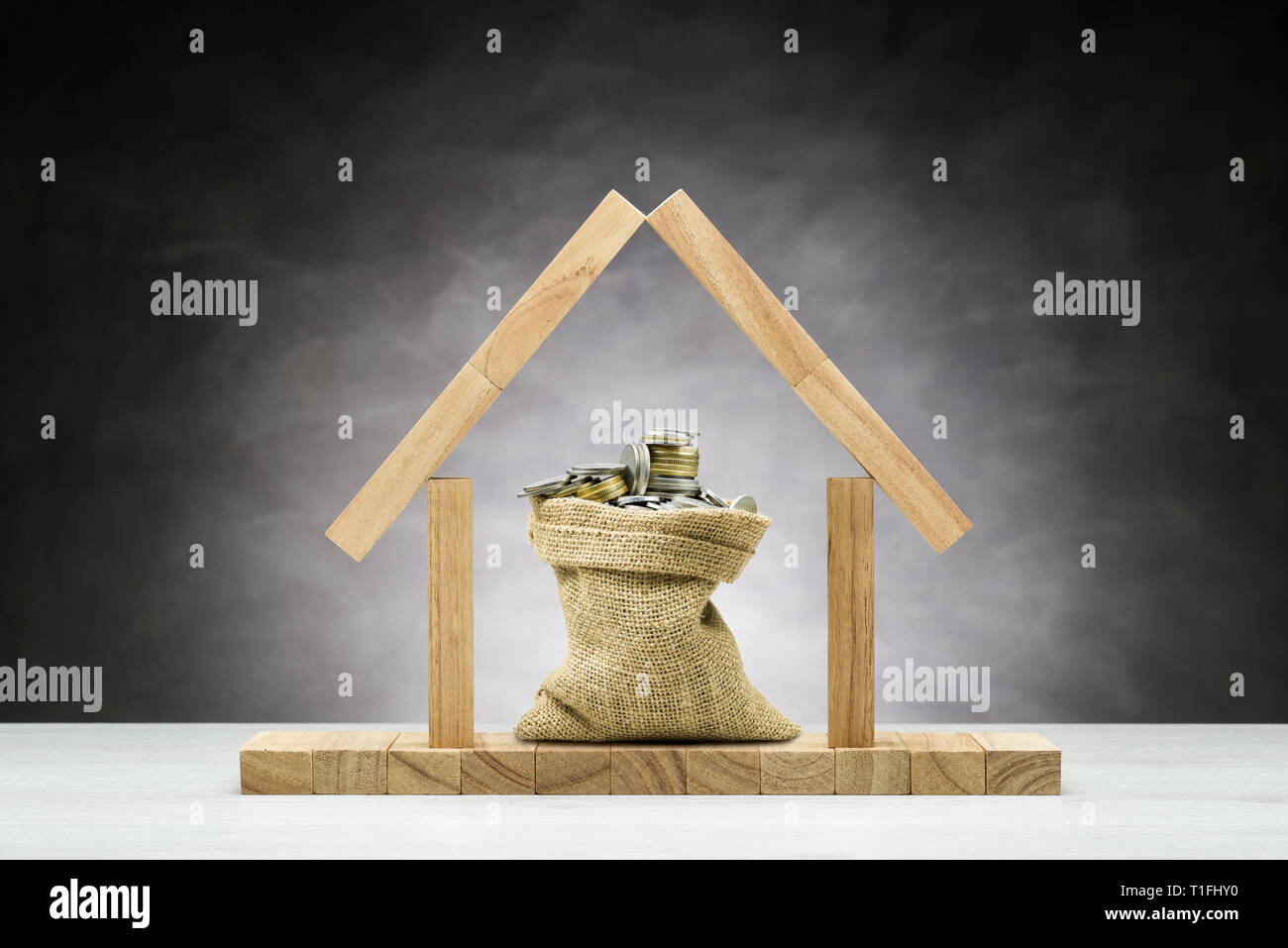 Concetto di protezione, casa in legno su uno sfondo grigio con borsa piena di monete sotto il tetto. Foto Stock