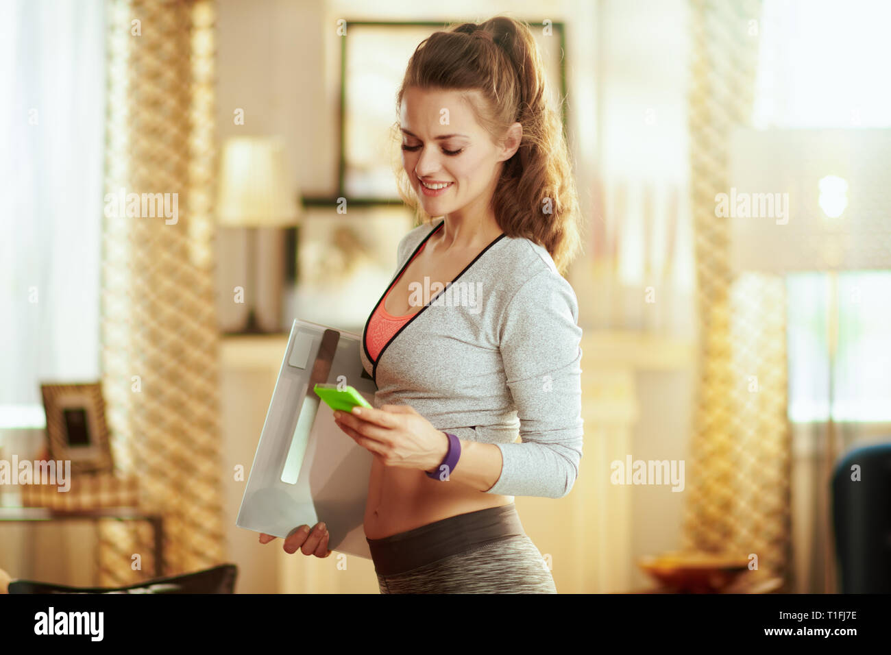 Felice donna sana in sport vestiti con scala smart utilizza lo smartphone per guardare in streaming fitness su internet in casa moderna. Foto Stock