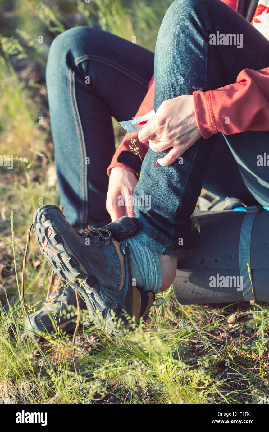 Giovane donna escursionista con zaino prendendo una calzatura off per inserire un intonaco aiuto sul suo piede dovuta alla stretta scarpa durante la vacanza in foresta Foto Stock