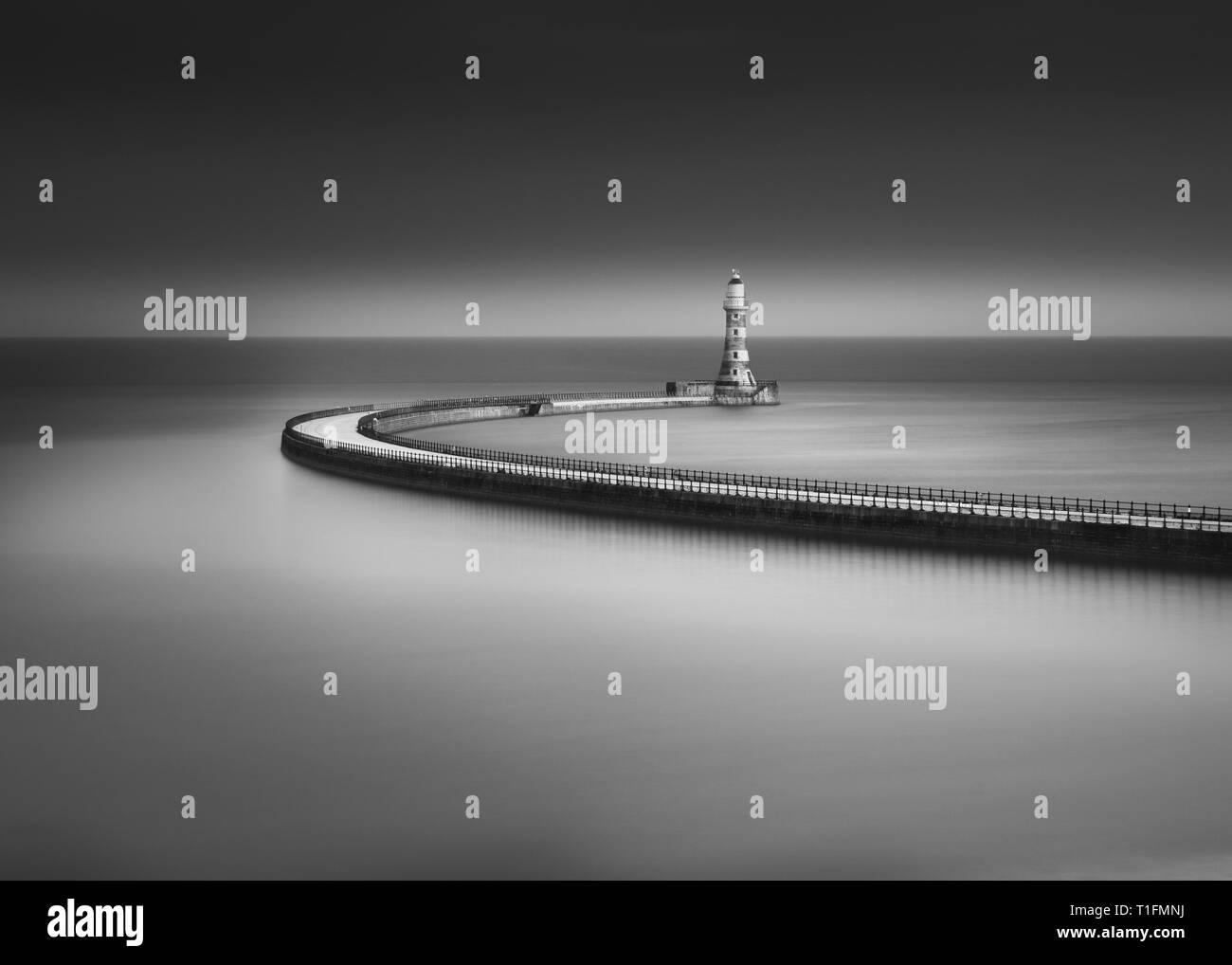 Un moody Arte in bianco e nero lunga esposizione di Roker Pier al tramonto con il lungo percorso di spazzamento dando un soft specchio di riflessione nel Mare del Nord Foto Stock