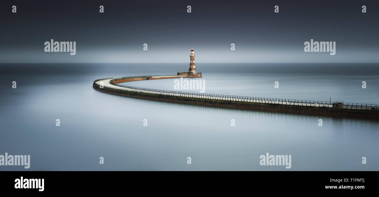 Un moody Arte colore lunga esposizione di Roker Pier al tramonto con il lungo percorso di spazzamento dando un soft specchio di riflessione nel Mare del Nord Foto Stock