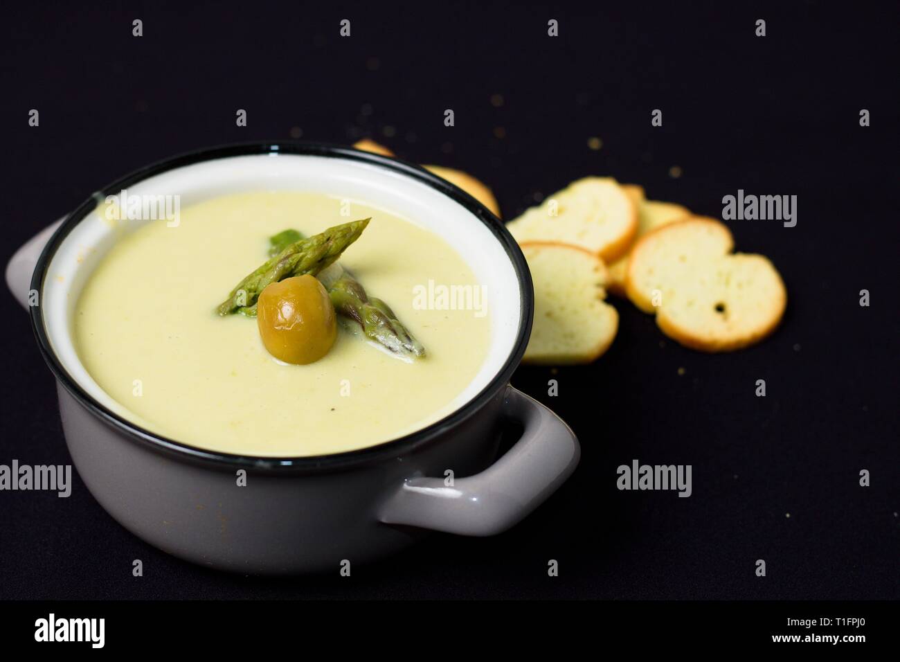 Cremosa zuppa di asparagi pieno di vitamine in grigio pot con olivi su sfondo nero Foto Stock