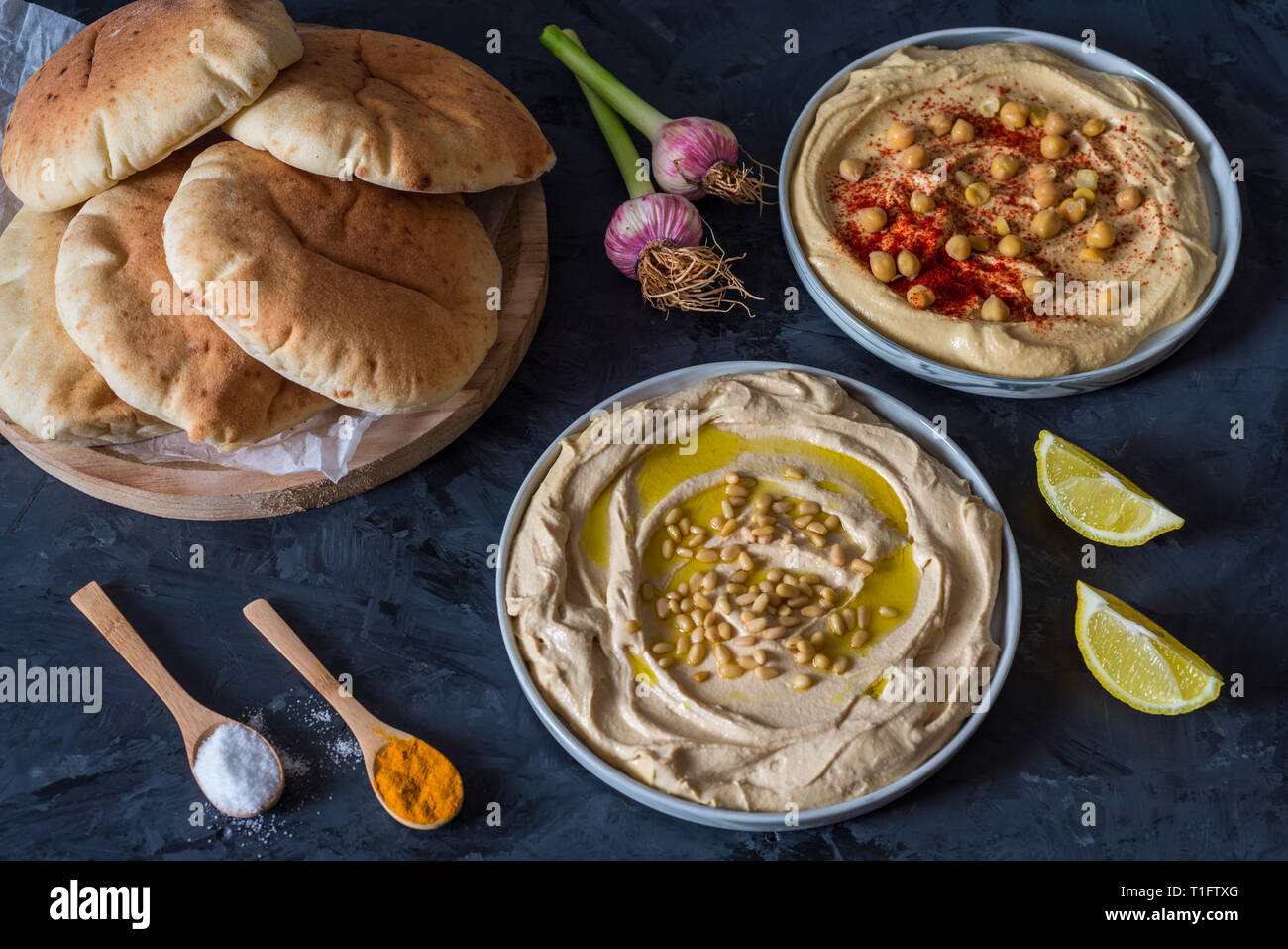 Piastre di hummus con pane pita su sfondo nero Foto Stock