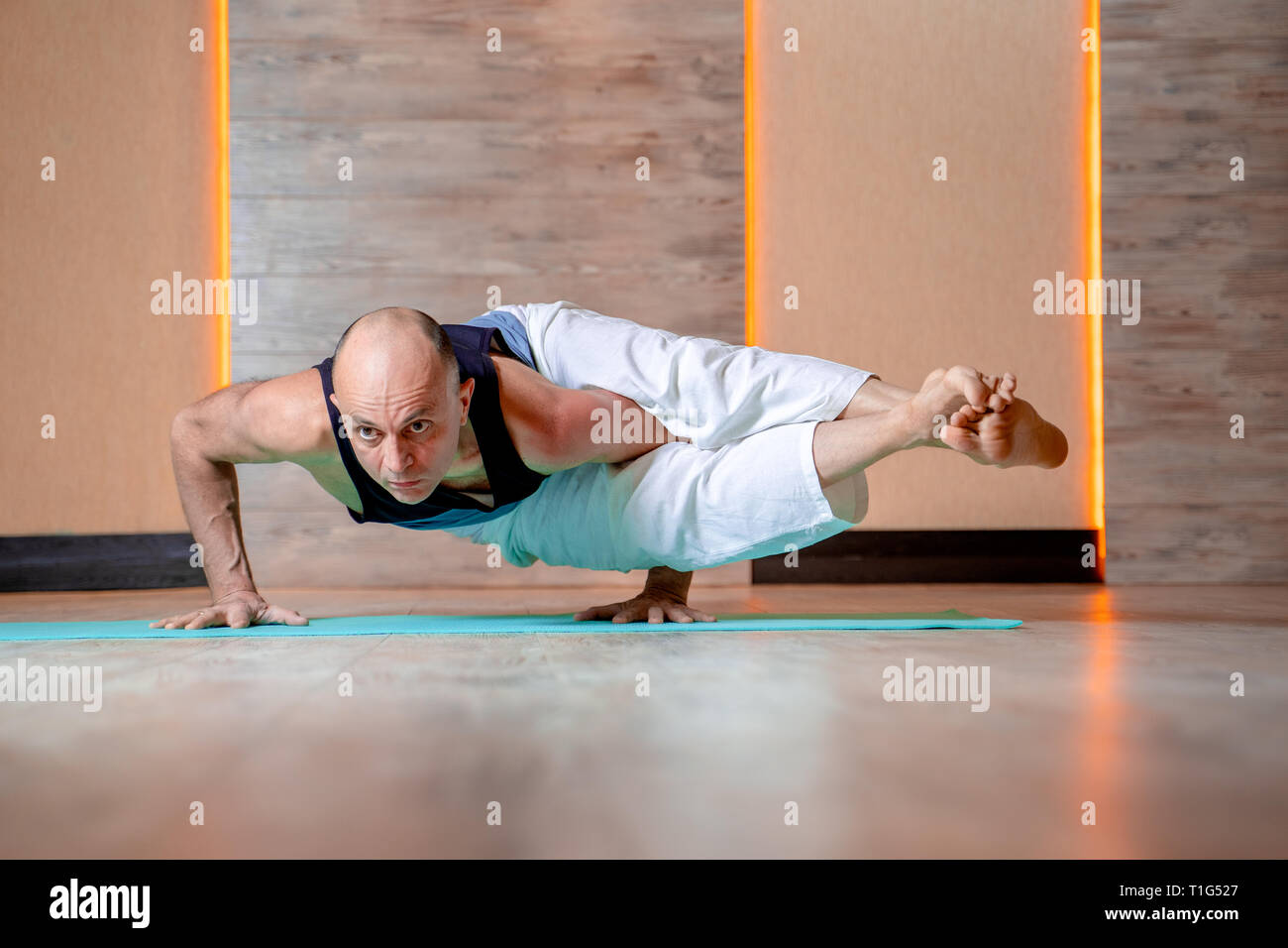 Atleta uomo le pratiche yoga mentre in piedi sulle mani sul tappetino blu . Foto Stock