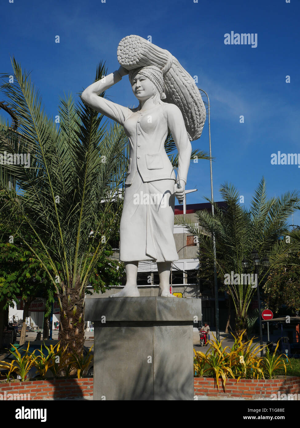 Battambang, Cambogia. Il raccolto di riso statua raffigura una donna in un mantello con un covone di riso bilanciato sulla sua testa e la falce in mano. Foto Stock