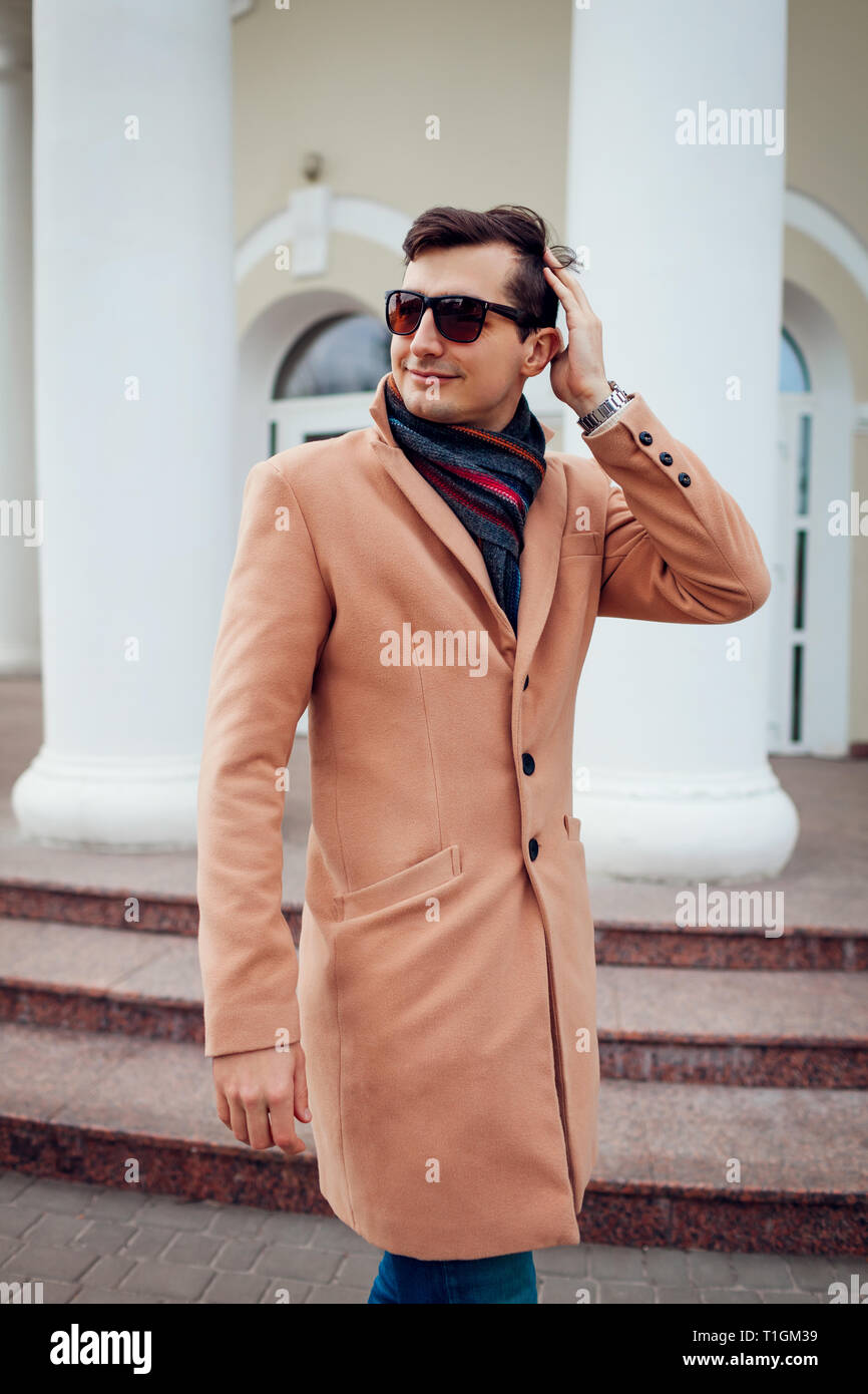 Giovane uomo elegante a piedi nella città. Bel ragazzo indossa abiti classici e accessori. Street fashion. Uomo di capelli di controllo Foto Stock