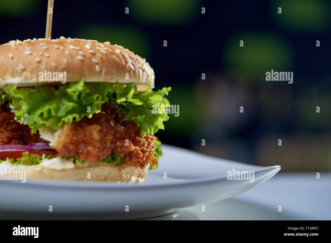 Primo piano della succosa burger con pollo fritto, verdure fresche, verdi e di sesamo e rimanendo sulla piastra in cafe. Grandi sandwich gustosi cotti per mangiare. Concetto di fast food e cucina. Foto Stock