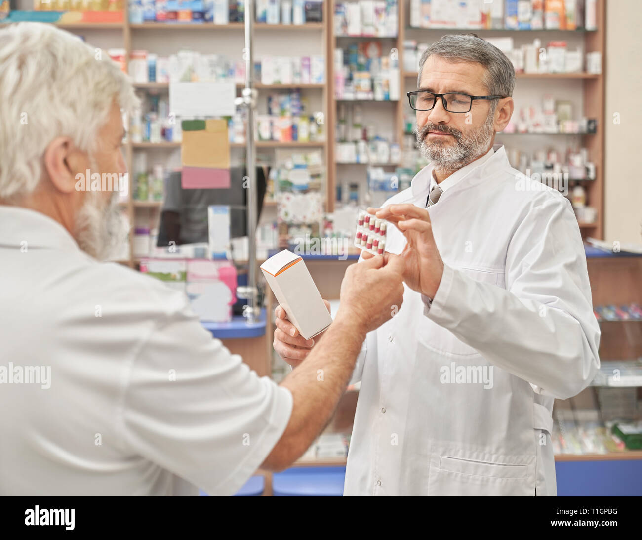 Il farmacista azienda blaster pack di pillole e cassetta medica. Specialista professionale aiutando pensionato a scegliere medicamnt in farmacia. Farmacia cliente consulenza in farmacia. Foto Stock
