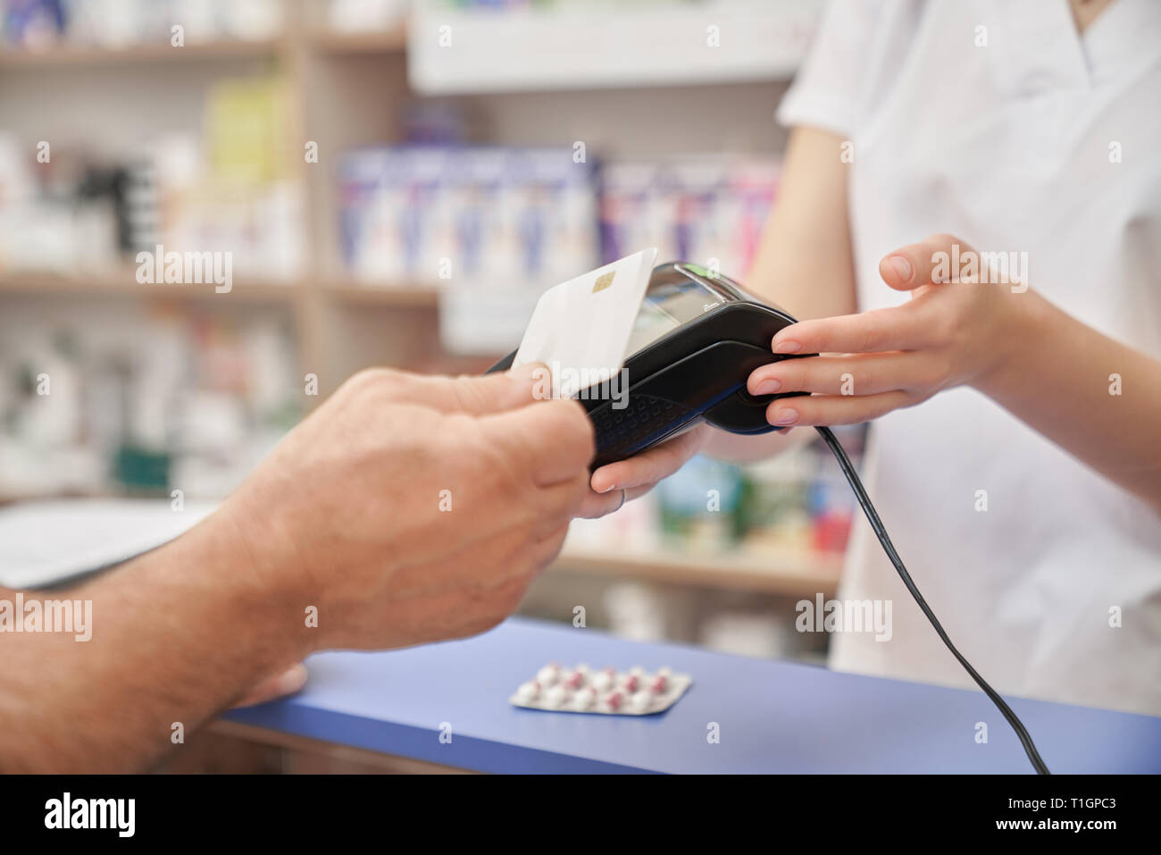 Il cliente effettuando il pagamento in farmacia. Il farmacista azienda terminale, uomo di pagare per i medicamenti con carta di credito. Pagamento moderno dalla macchina, Blister di pillole sul contatore. Foto Stock