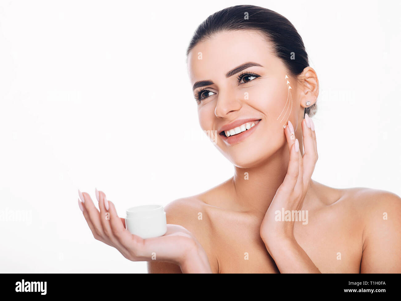 Donna sorridente con frecce di sollevamento sulla faccia di applicare una crema idratante sulla pelle. Concetto di crema idratante lifting della pelle Foto Stock