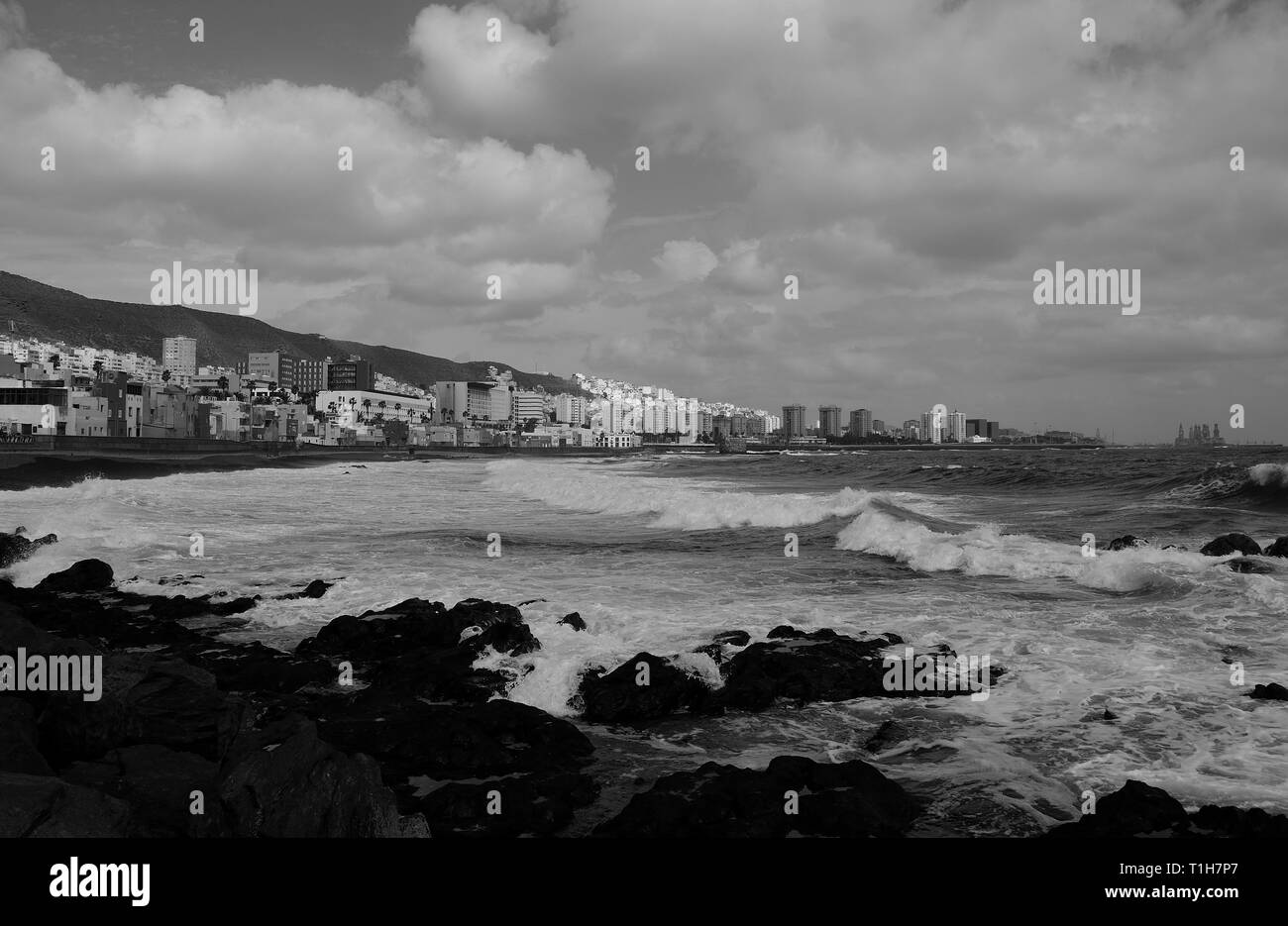 Costa rocciosa con mare mosso, città e cielo nuvoloso, Las Palmas de Gran Canaria, effetto bianco e nero, Isole Canarie Foto Stock