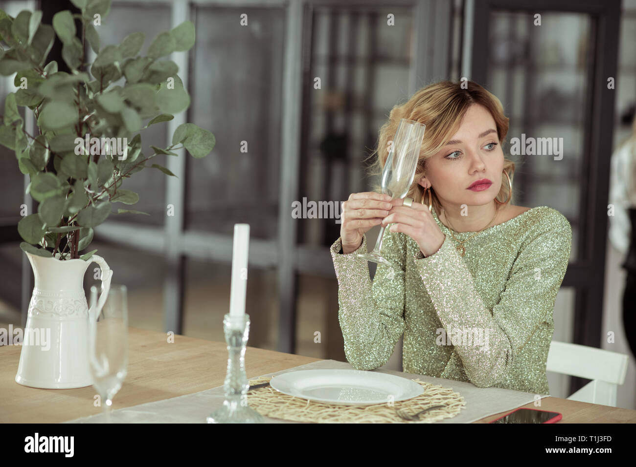 Giovane moglie seduto da solo al tavolo con candele e bicchieri Foto Stock